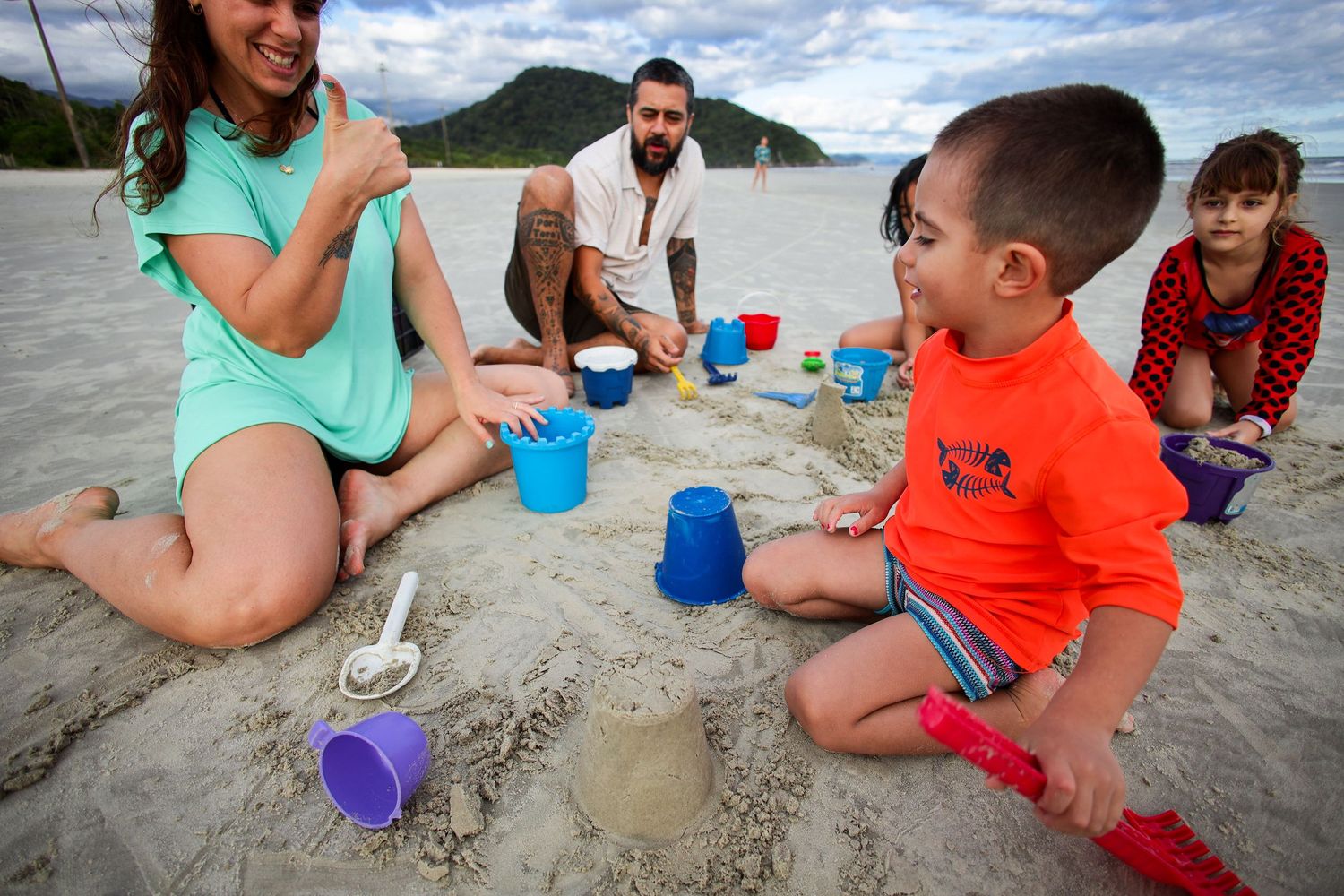 Children playing and building sandcastles on a sandy beach with colorful buckets and toys.