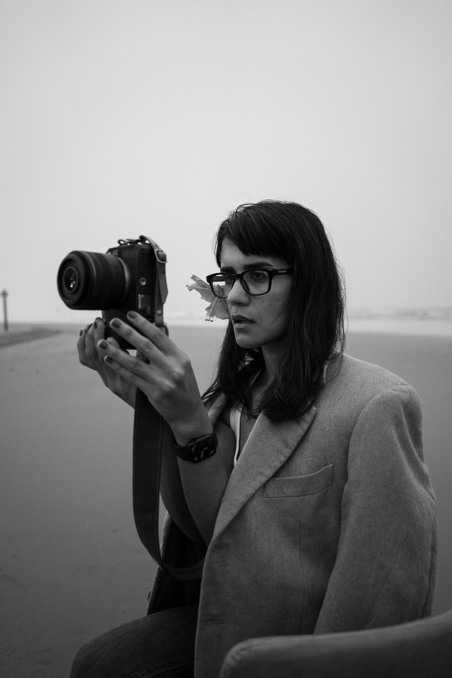 Black and white portrait of a photographer wearing glasses and blazer holding a digital camera outdoors.