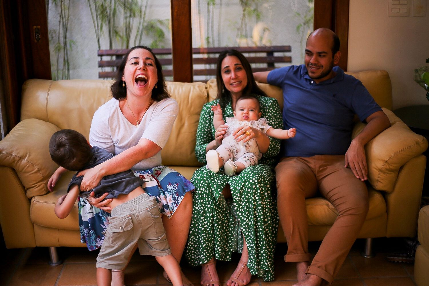 Group enjoying a lighthearted moment together on a tan leather couch in a living room with bamboo decor in background.