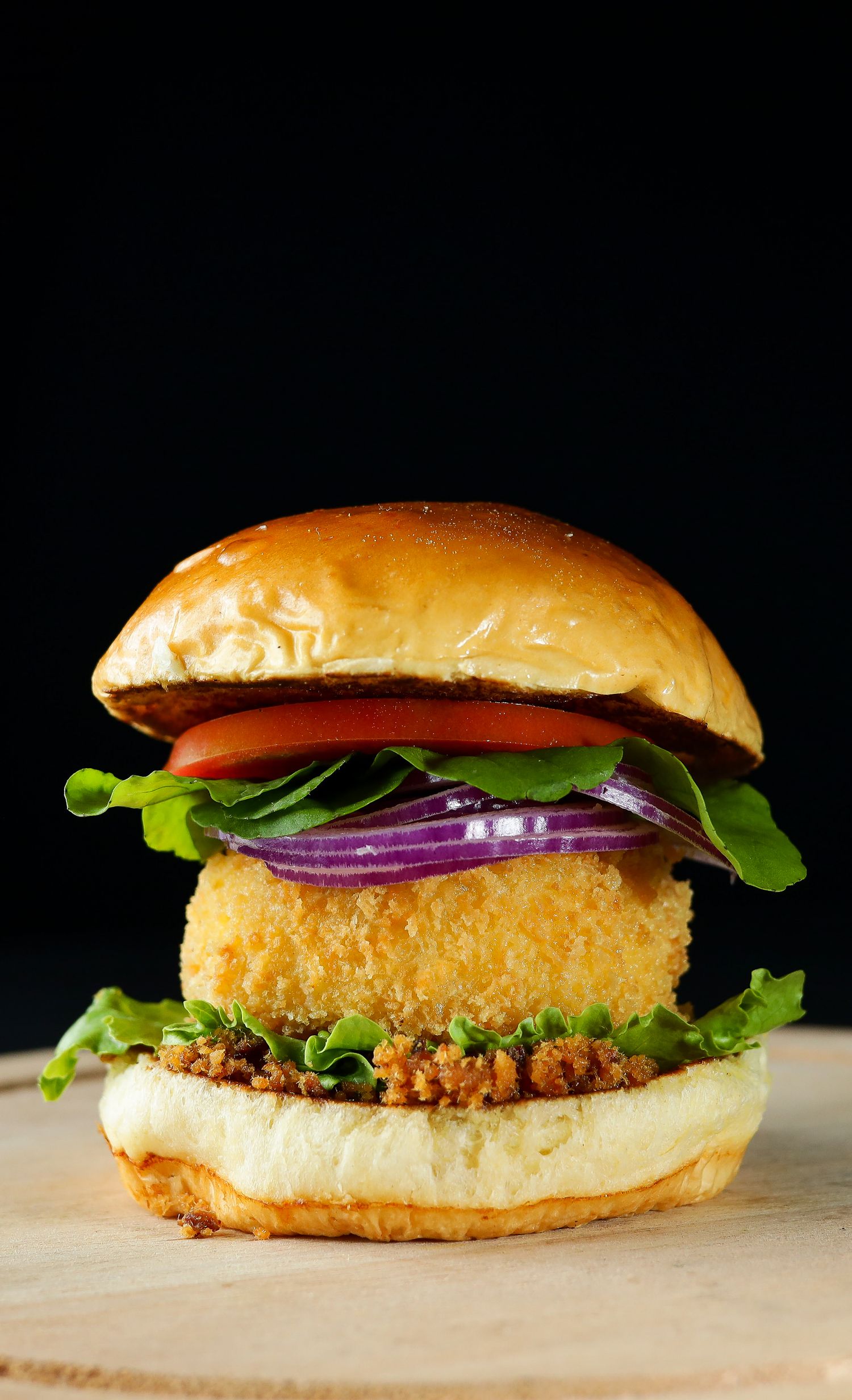 A crispy breaded chicken sandwich with lettuce, tomato, red onion, and sauce on a golden brioche bun.