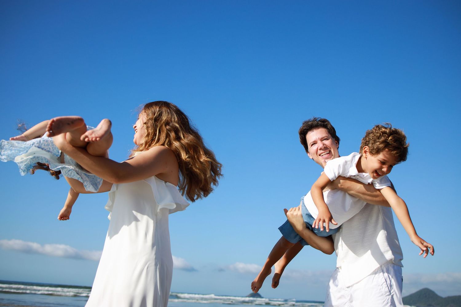 Joyful beach scene of people playing and lifting others against blue sky background.