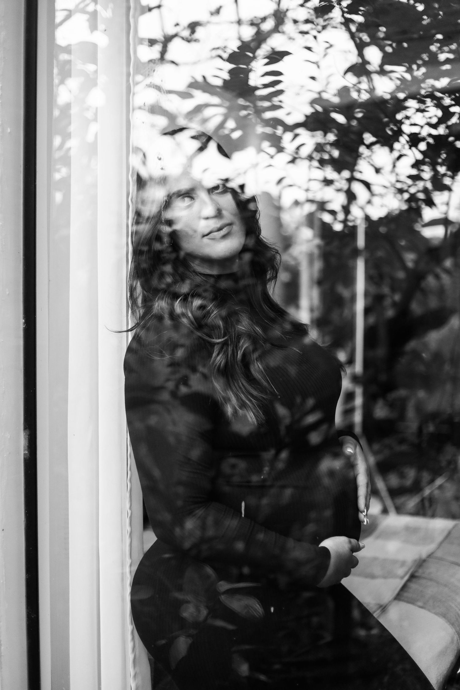 A black and white portrait shot through a window with shadows of leaves and foliage creating a dreamy pattern overlay.