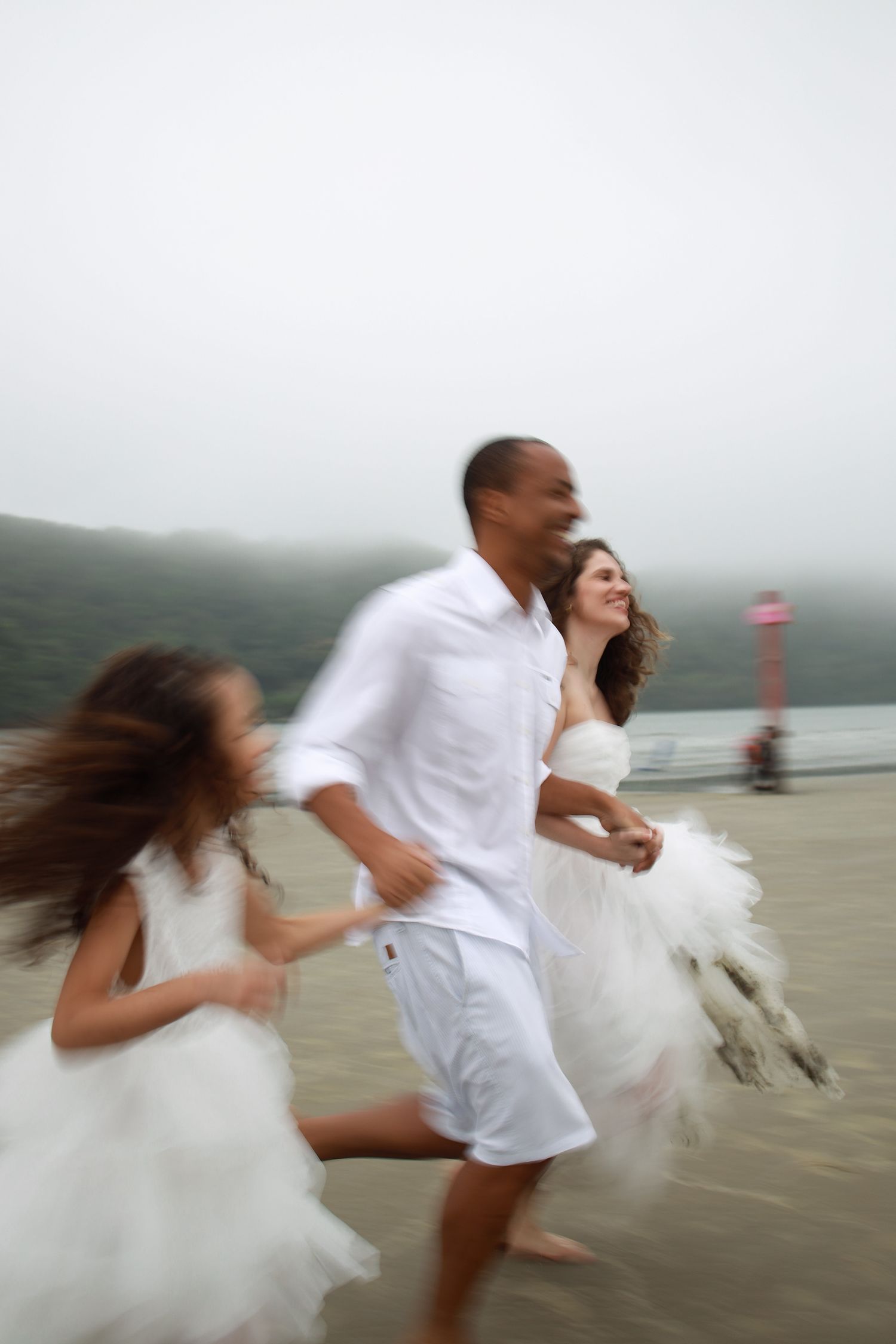 A blurred motion shot of a family in white clothing running joyfully together on a misty beach.