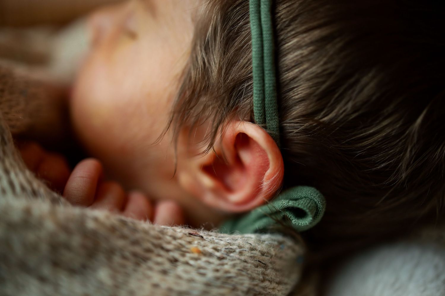 Close-up view of a child's ear with a green string or cord visible, wearing a knit sweater.