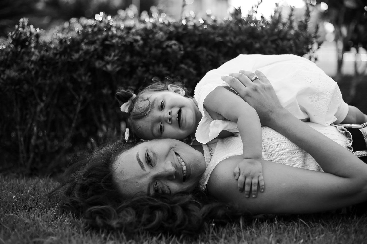 A black and white photograph of a tender moment shared between family members lying in the grass outdoors.