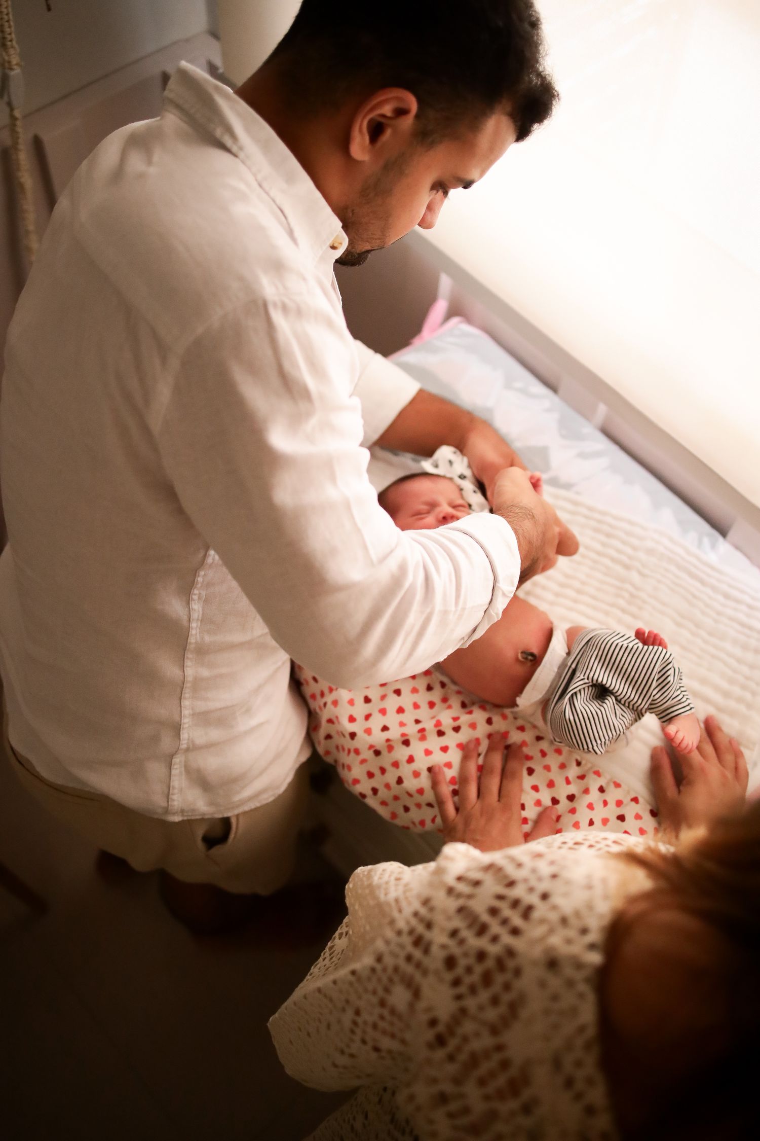 A gentle moment of someone in a white shirt tenderly caring for a baby wearing polka dot clothing on a bed.