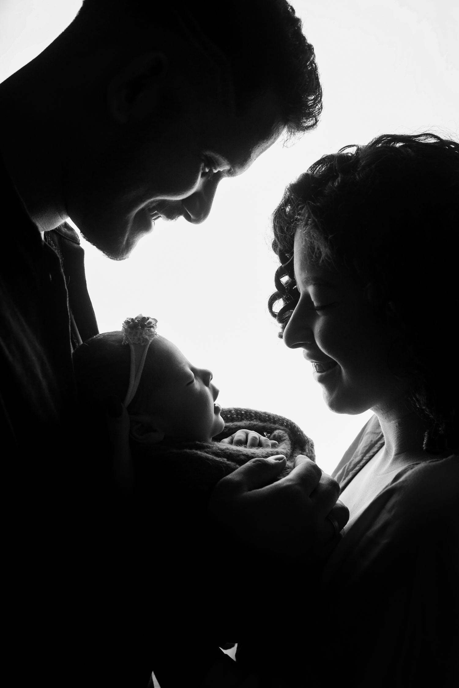 Black and white silhouette photograph of a couple tenderly holding their newborn baby in an intimate family moment.