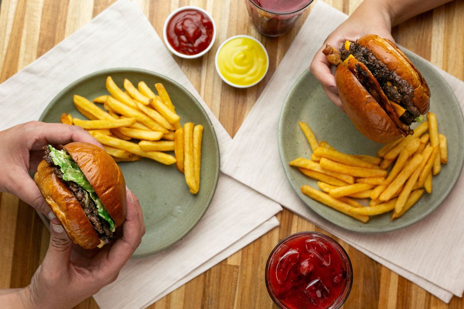 Fresh cheeseburgers served on green plates with crispy french fries and condiments on a wooden table.
