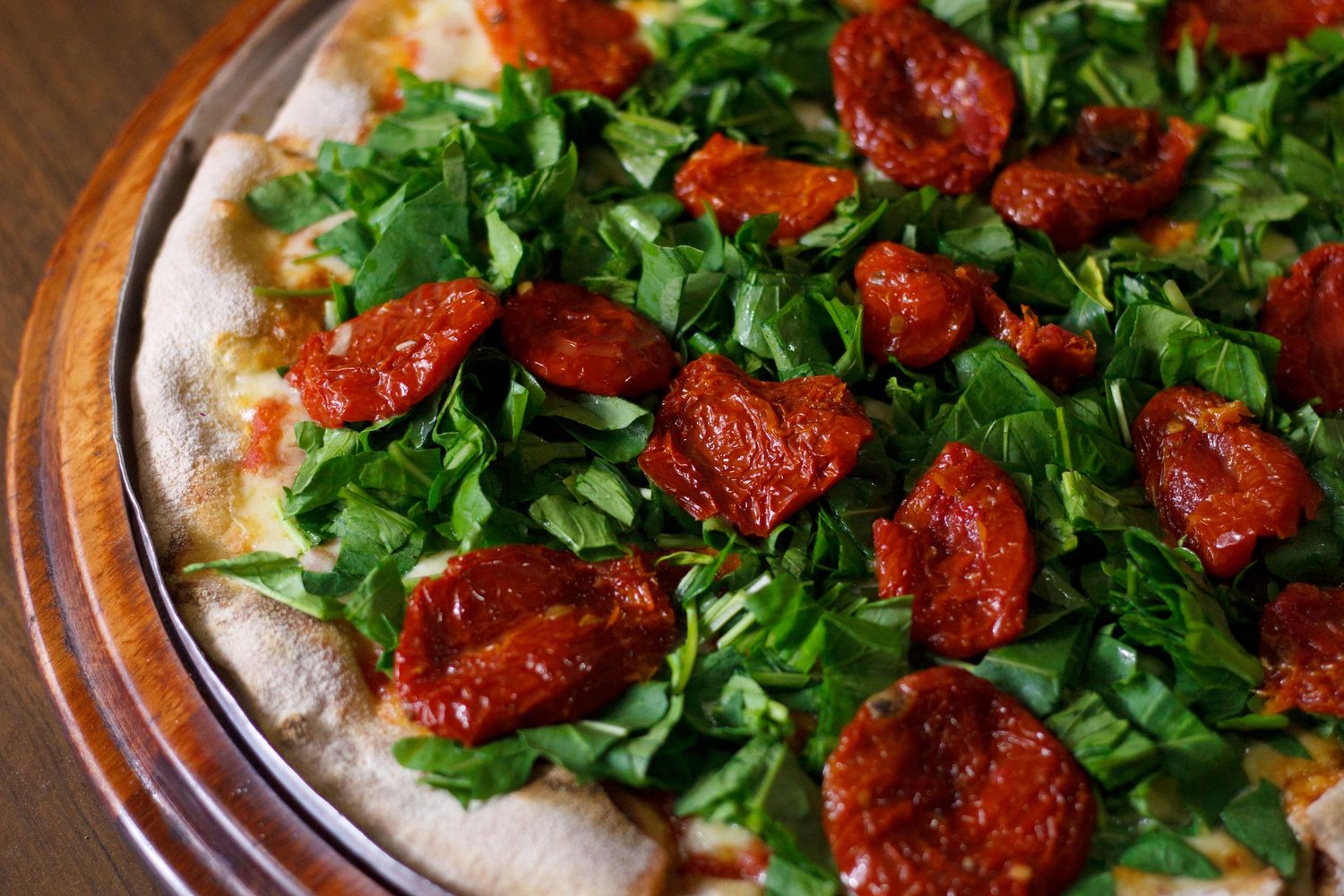 A rustic pizza topped with fresh arugula and roasted cherry tomatoes served on a wooden board.
