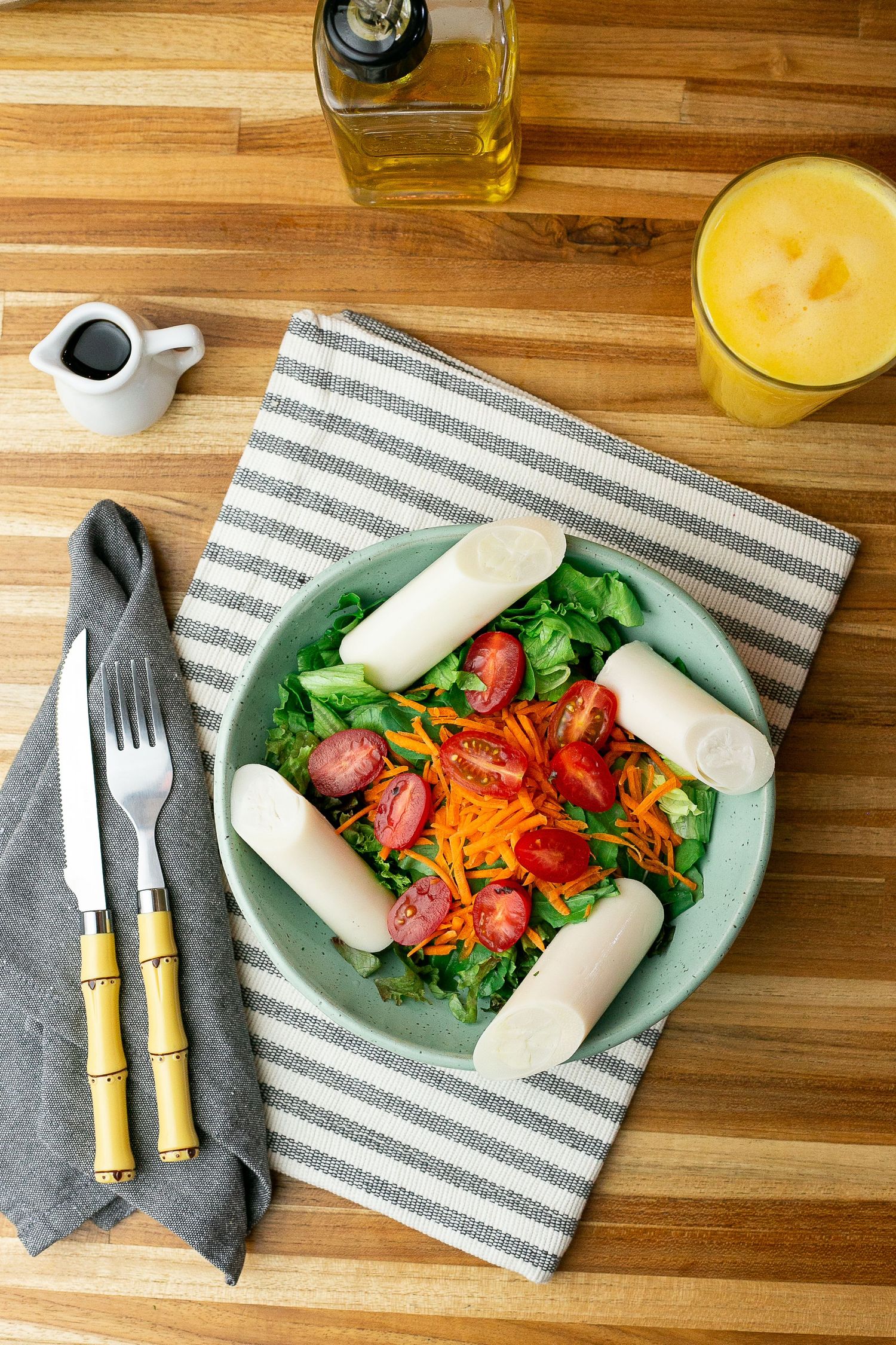 Fresh garden salad with sliced tomatoes and white mozzarella sticks served on green plate with orange juice and utensils.