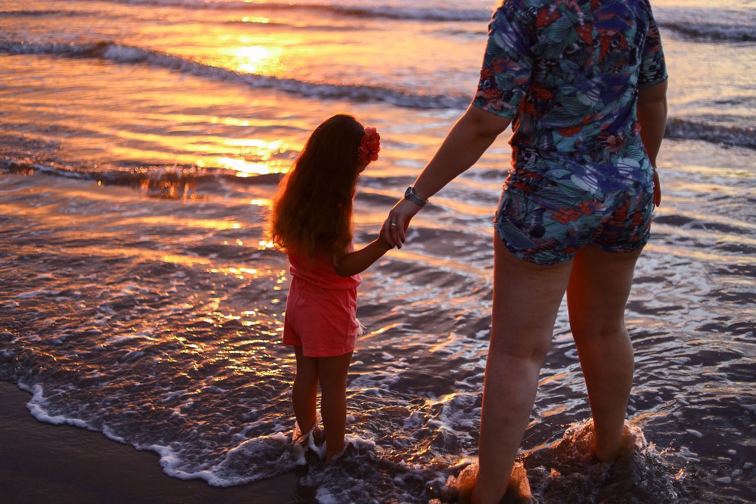 Silhouettes near the water's edge during a vibrant orange sunset at the beach reflect in rippling waves.
