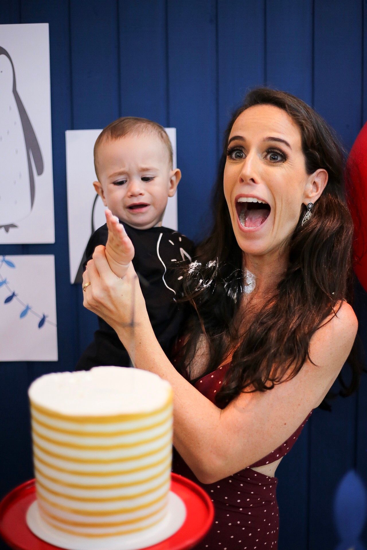 People sharing a joyful moment near a striped birthday cake against a blue wall with penguin artwork.