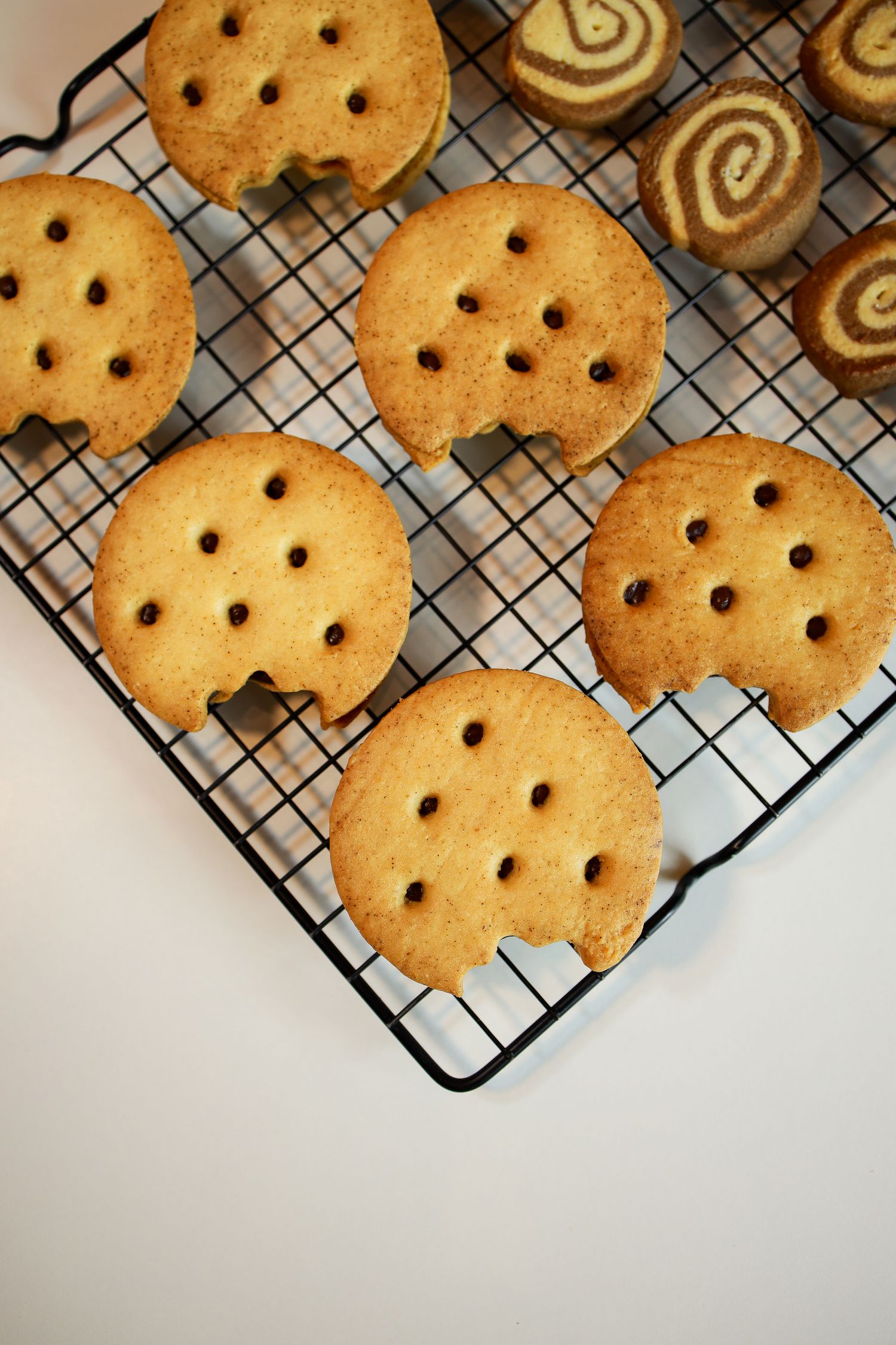 Homemade sugar cookies with fork-pressed holes cooling on a wire rack next to pinwheel cookies.