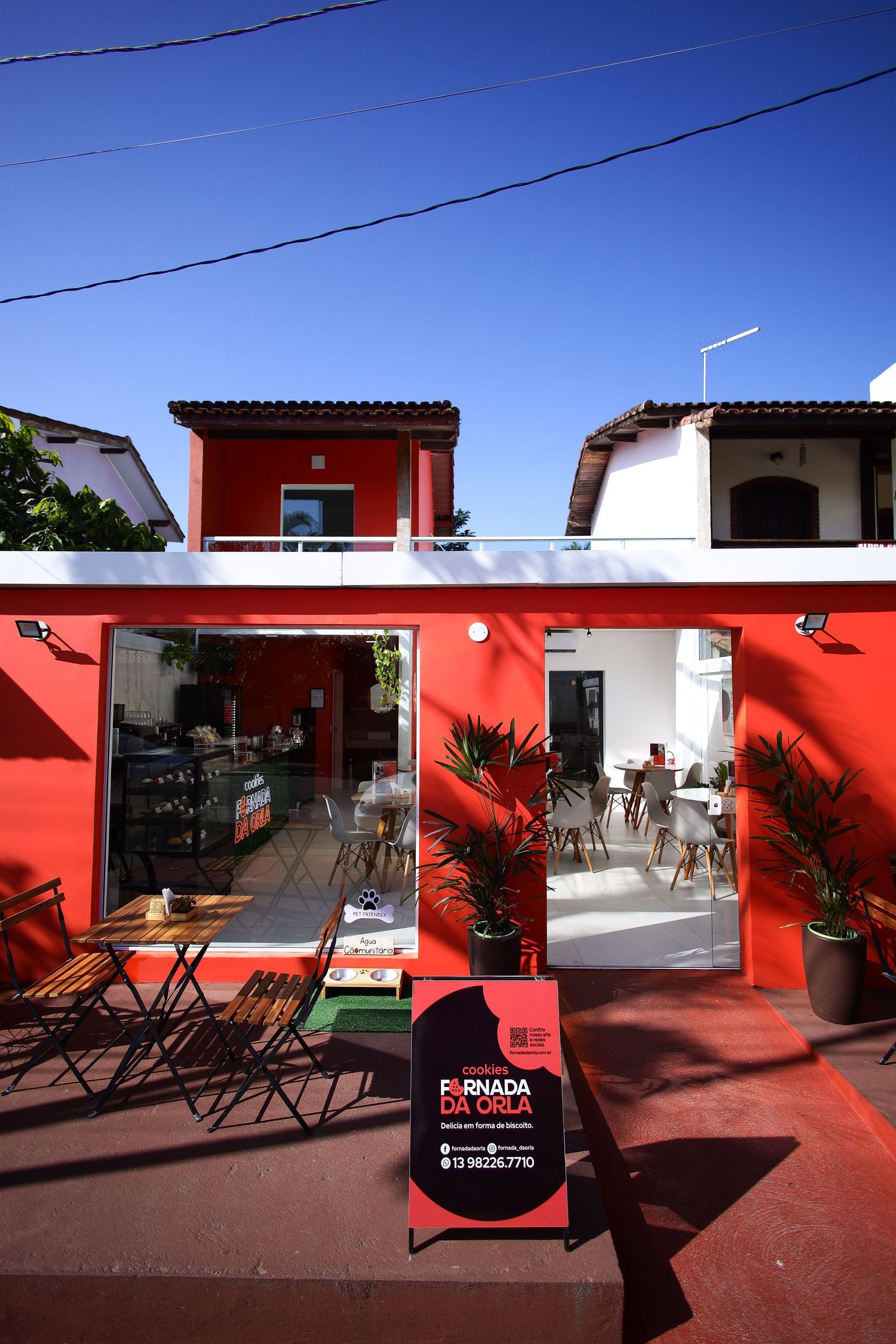 Vibrant red and white cafe storefront with outdoor seating and palm plants under bright blue sky in Mediterranean style.