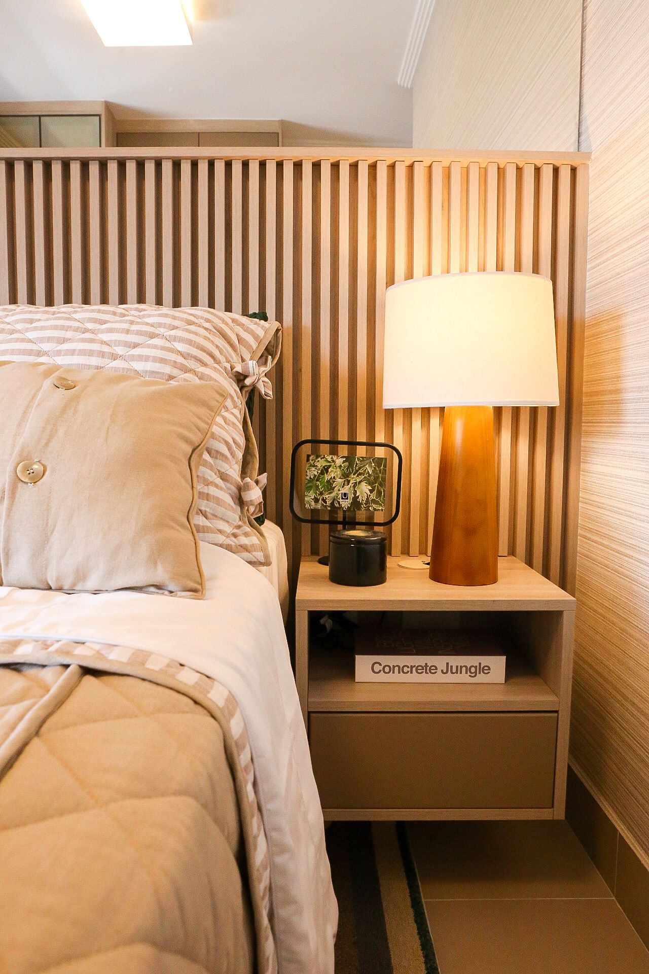 Modern bedroom interior with wooden slat wall, white bedding, and minimalist table lamp on nightstand.