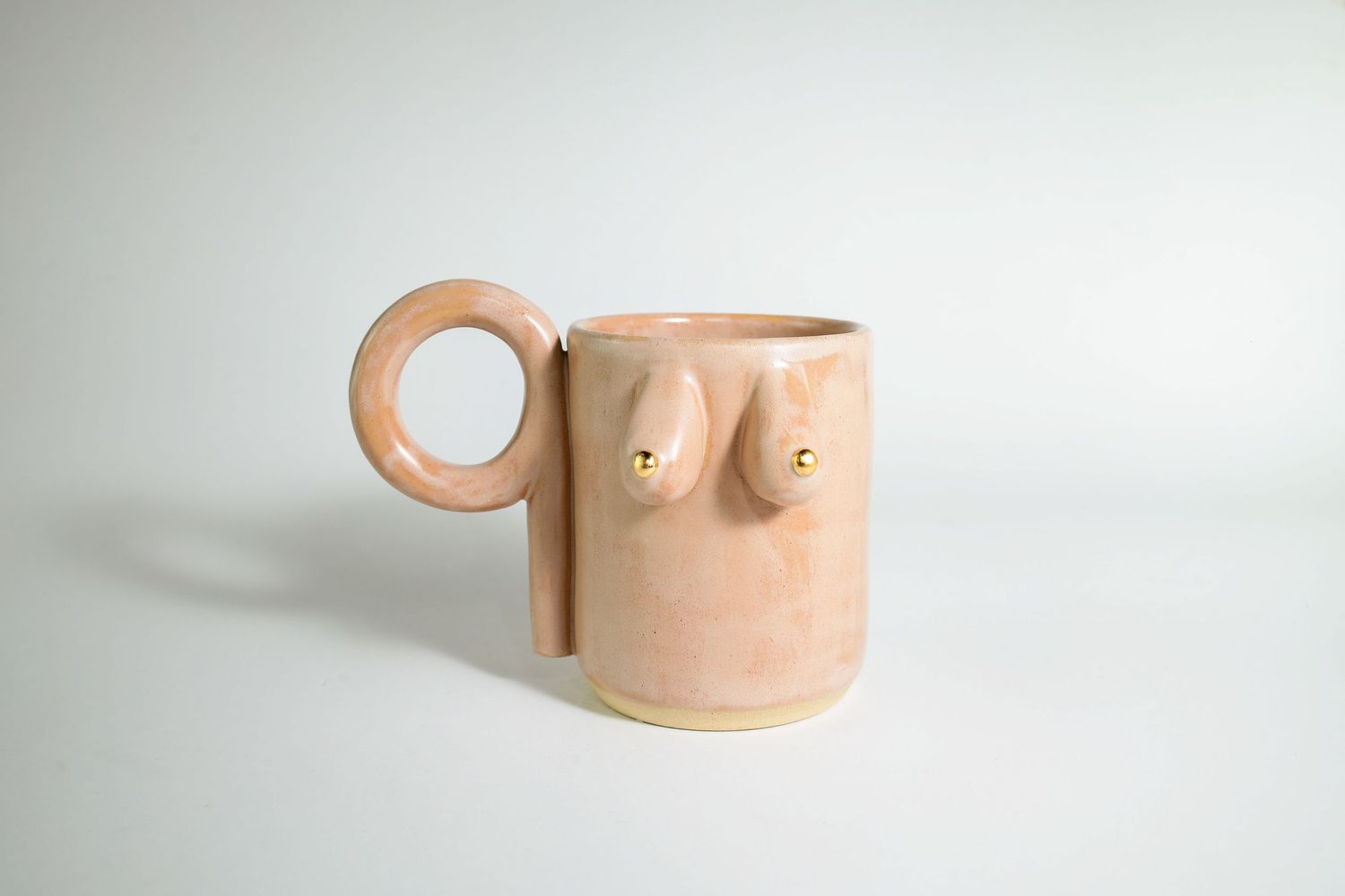 Handcrafted ceramic mug with minimalist face design features a peach-colored glaze and distinctive circular handle.