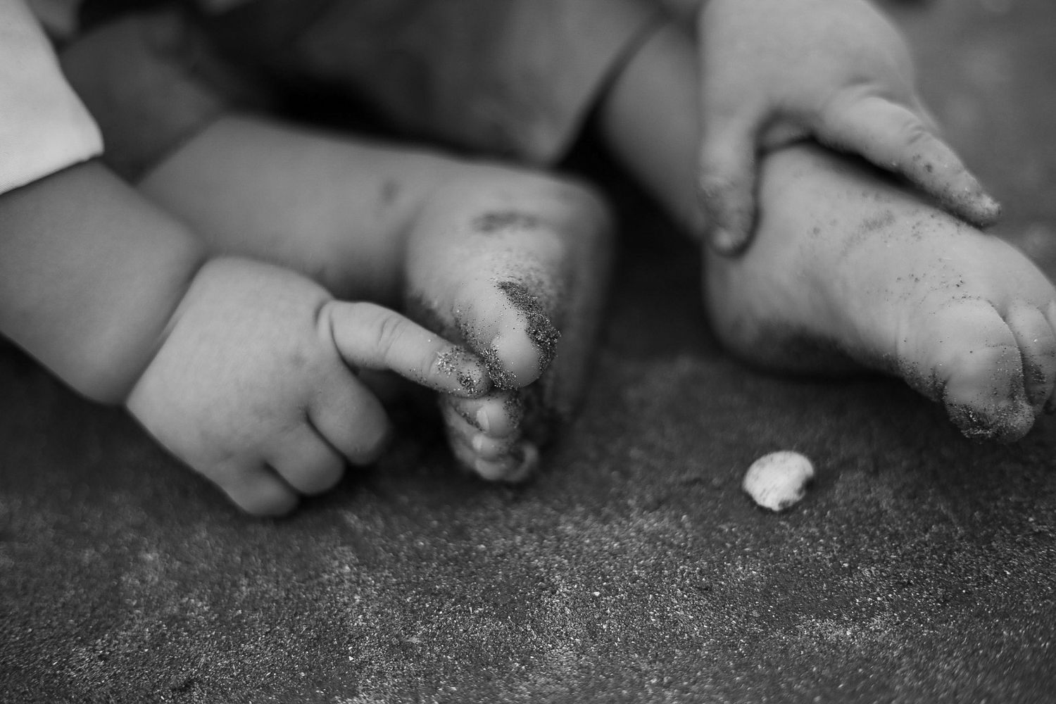 Black and white photograph of small dirty feet on the ground with a piece of white chalk.