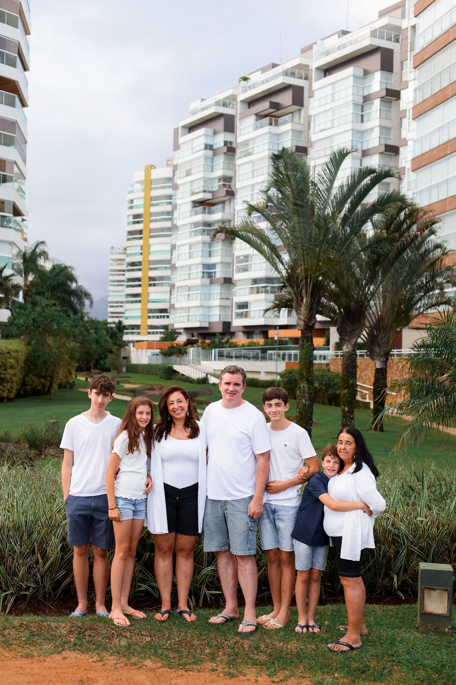 A group stands together on a grassy lawn near tropical palm trees with modern apartment buildings in the background.