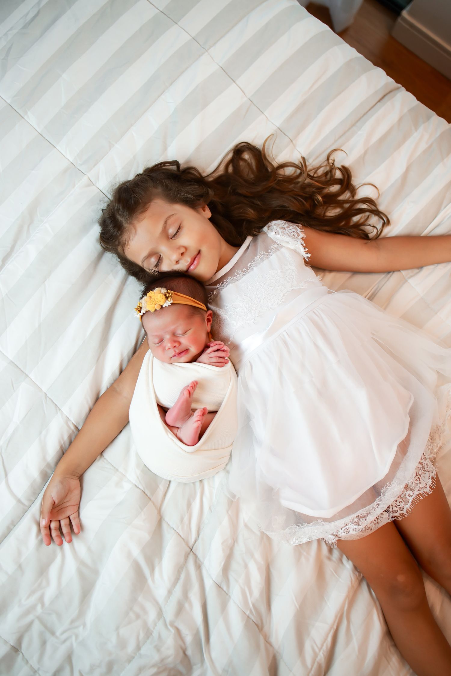 Two people in white dresses lying peacefully on white bedding viewed from above.
