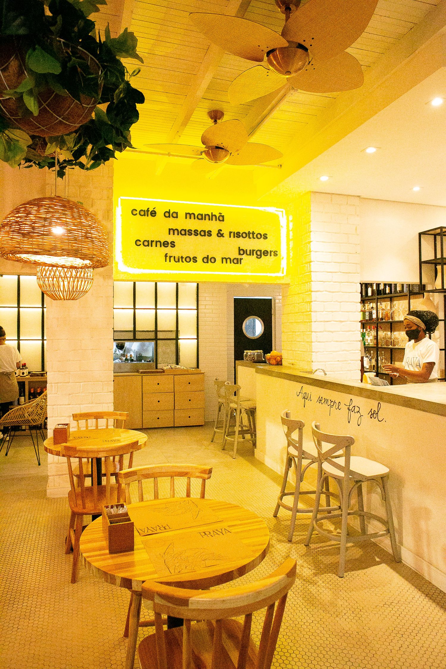Modern cafe interior with wooden tables, woven pendant lights, yellow signage and white tiled walls creates a warm ambiance.