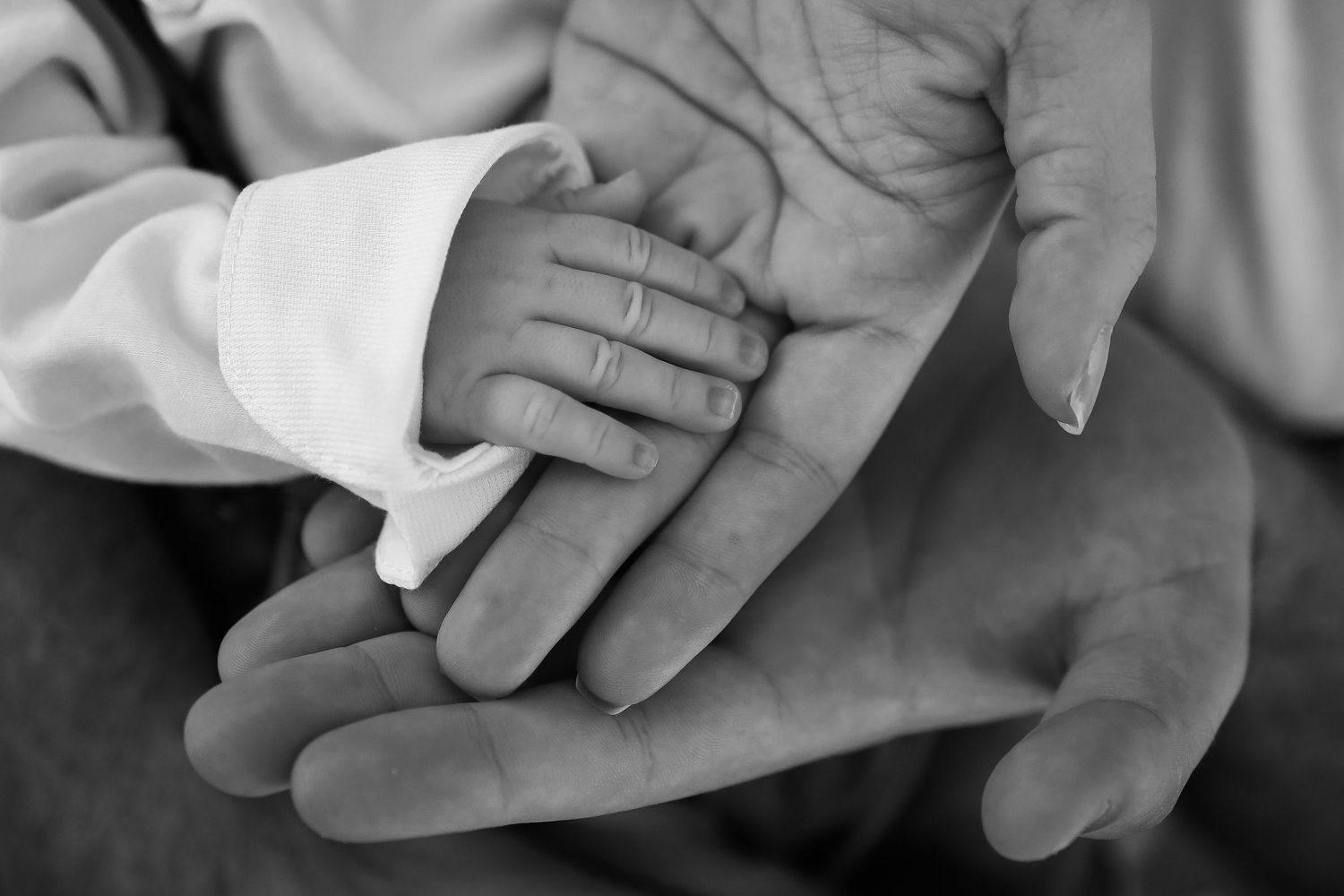 A tiny baby hand gently holds an adult's finger in a tender black and white portrait.