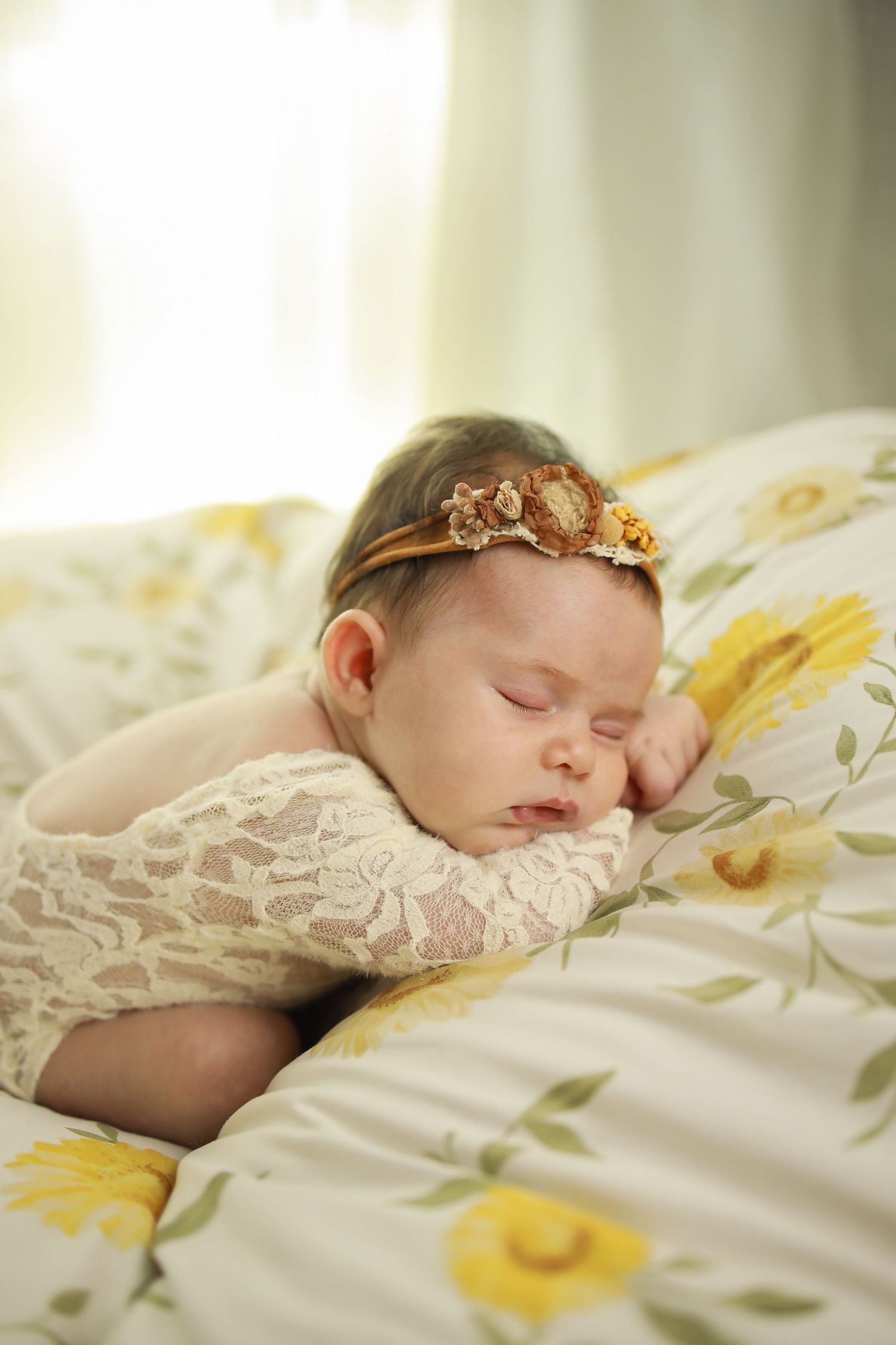 A sleeping newborn baby wearing a delicate headband rests peacefully on floral bedding.