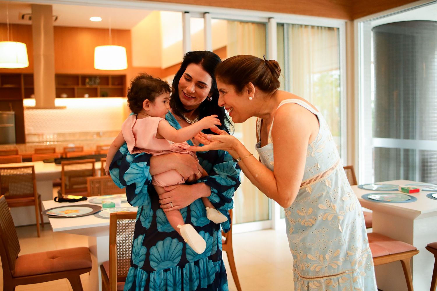 Three people share a heartwarming moment while interacting with a small child in a cozy dining room setting.