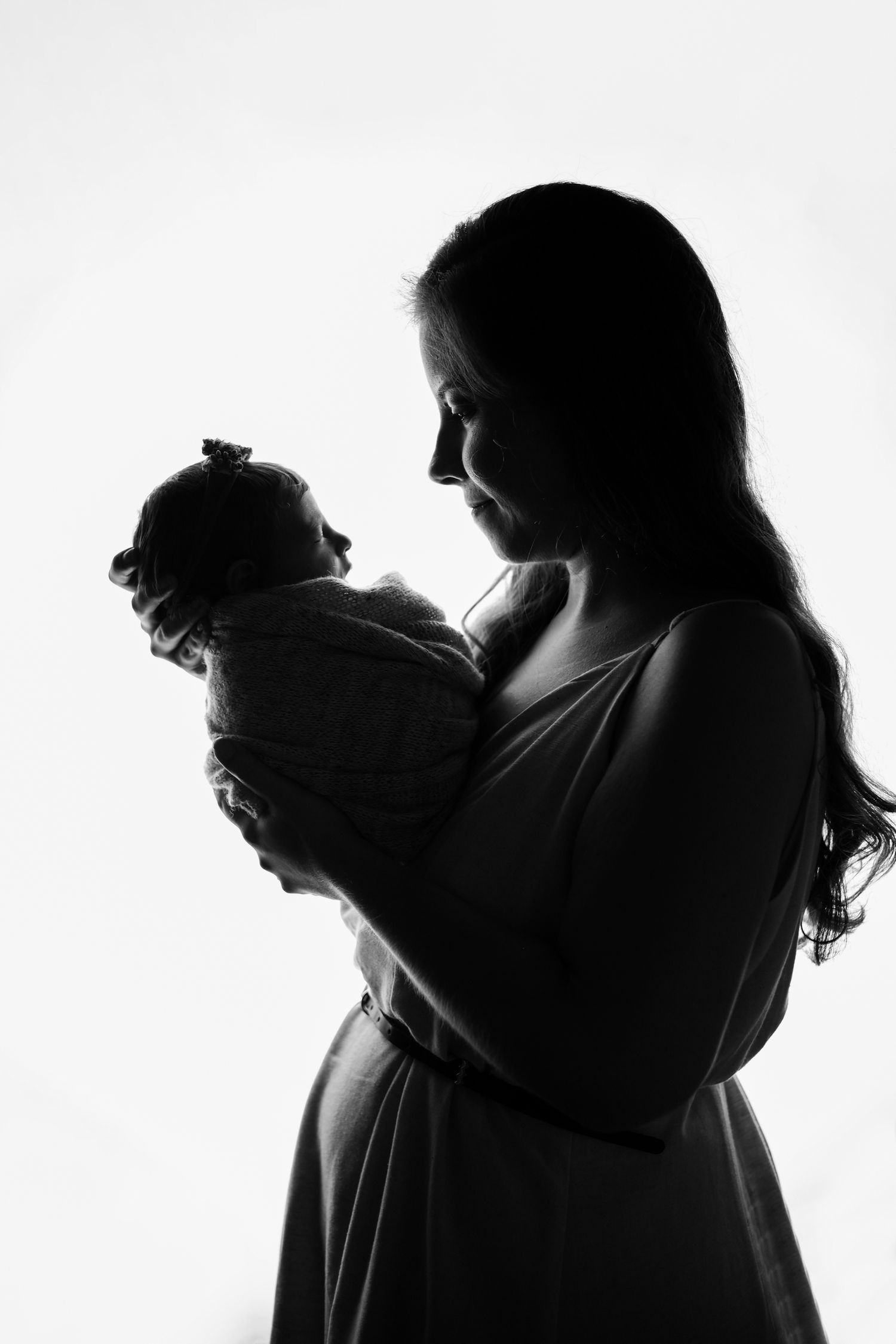 A silhouette profile of a parent tenderly holding a baby in black and white photography.