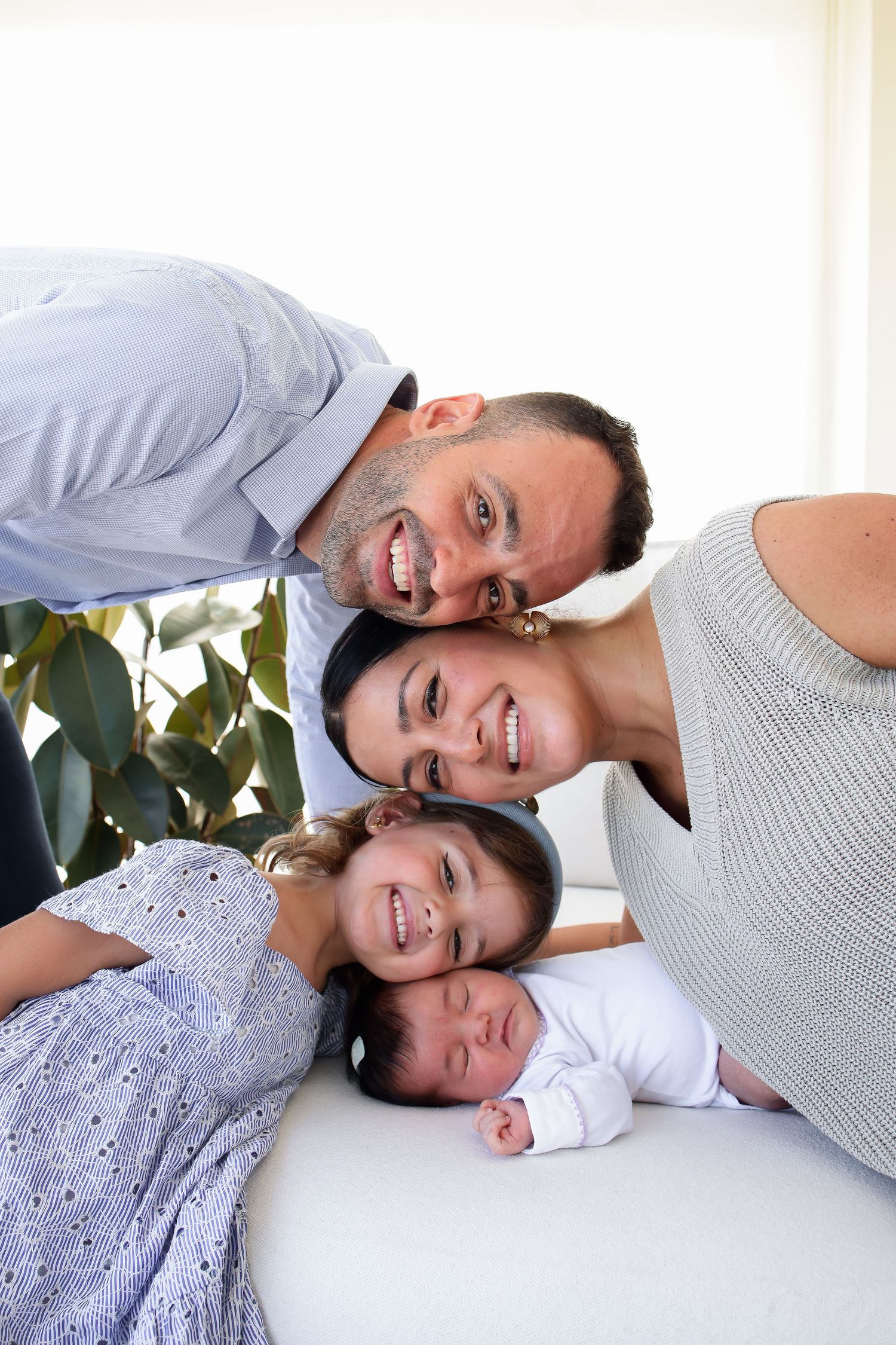 A happy family poses together on a bright white background with a green plant in the corner.