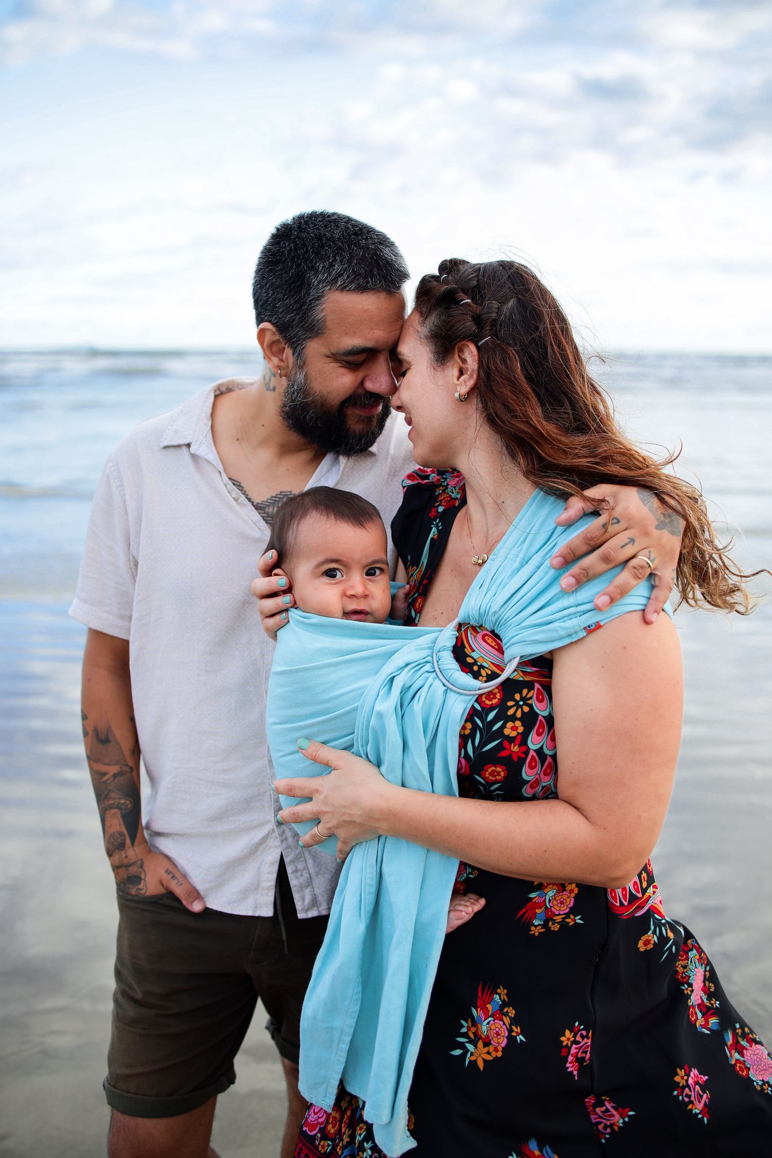Family enjoying tender moments together on a cloudy beach with gentle waves in the background.