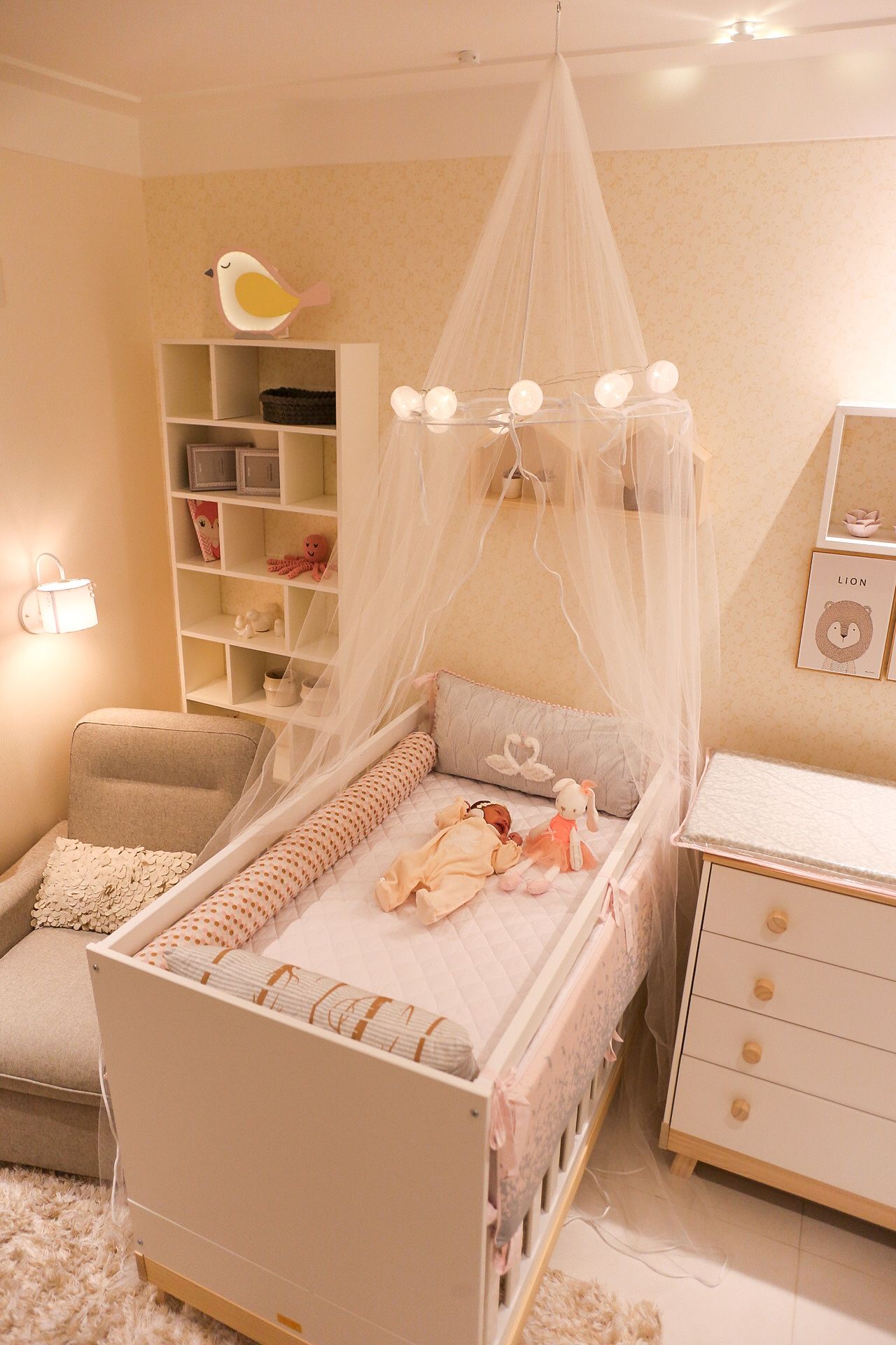 Cozy nursery room with white canopy bed, bookshelf, soft lighting, and pink and beige color scheme.