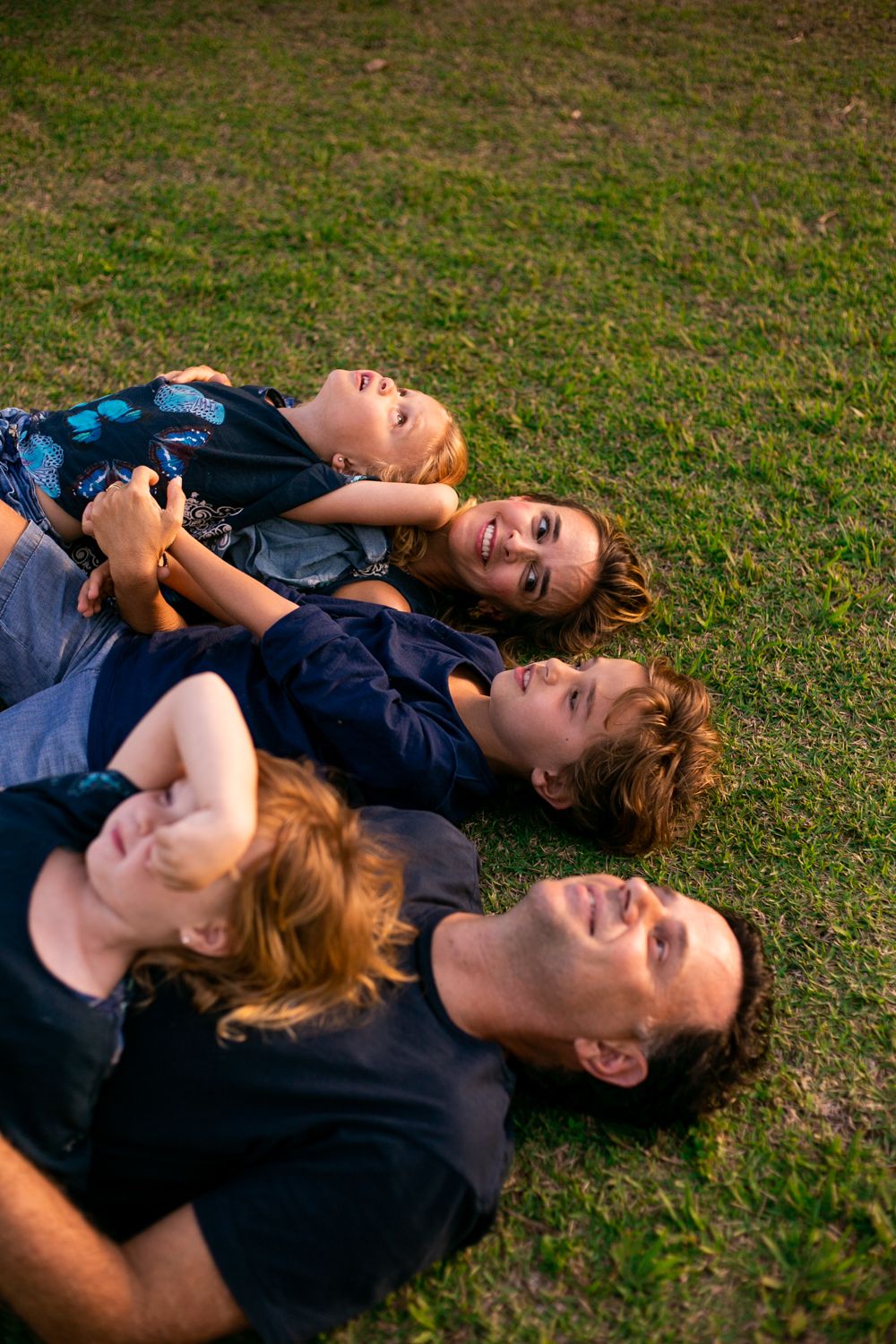 Group of people lying on grass together while smiling and laughing on a sunny day outdoors.