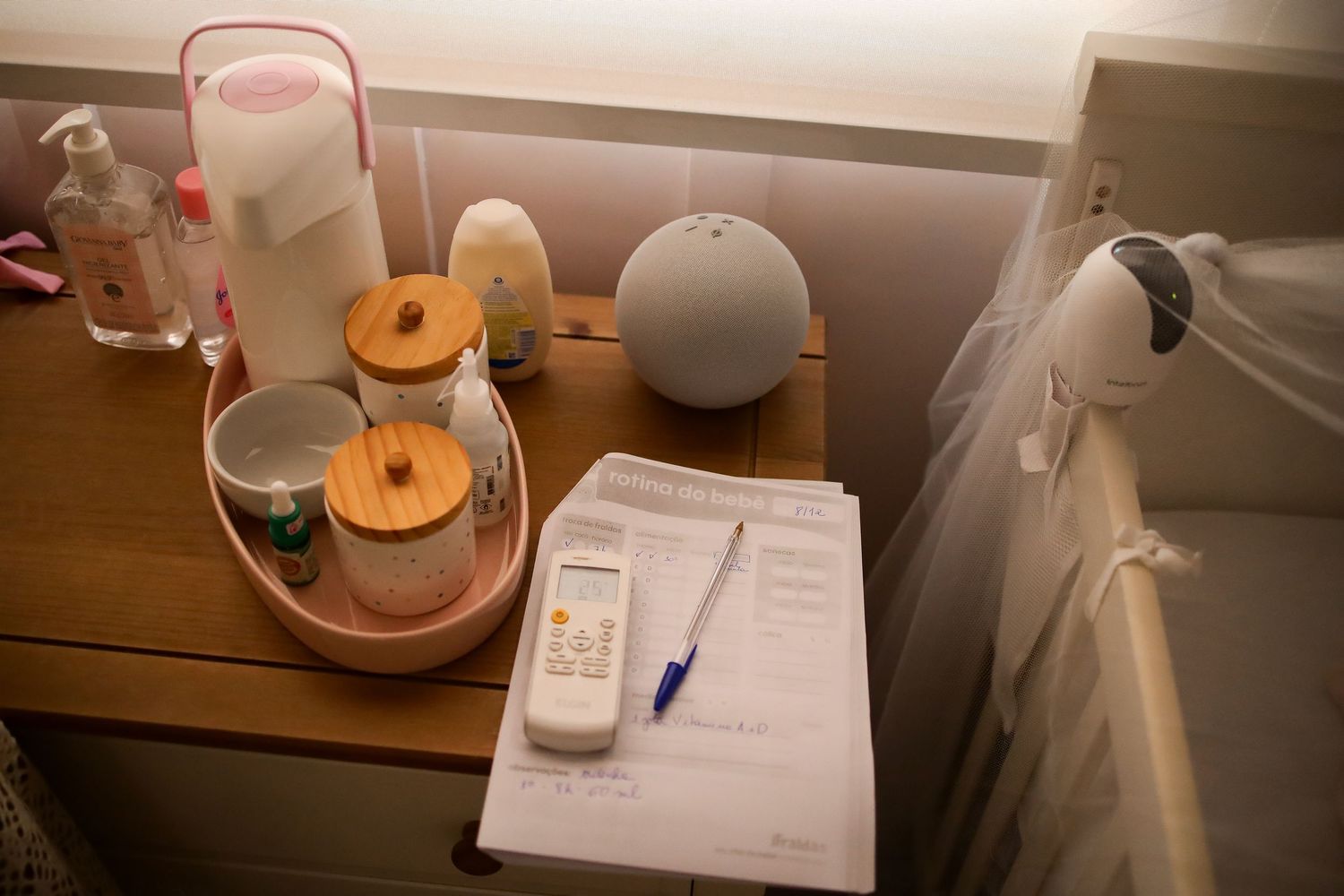 A wooden bedside table with two donuts on a plate, paperwork, and a white spherical lamp.
