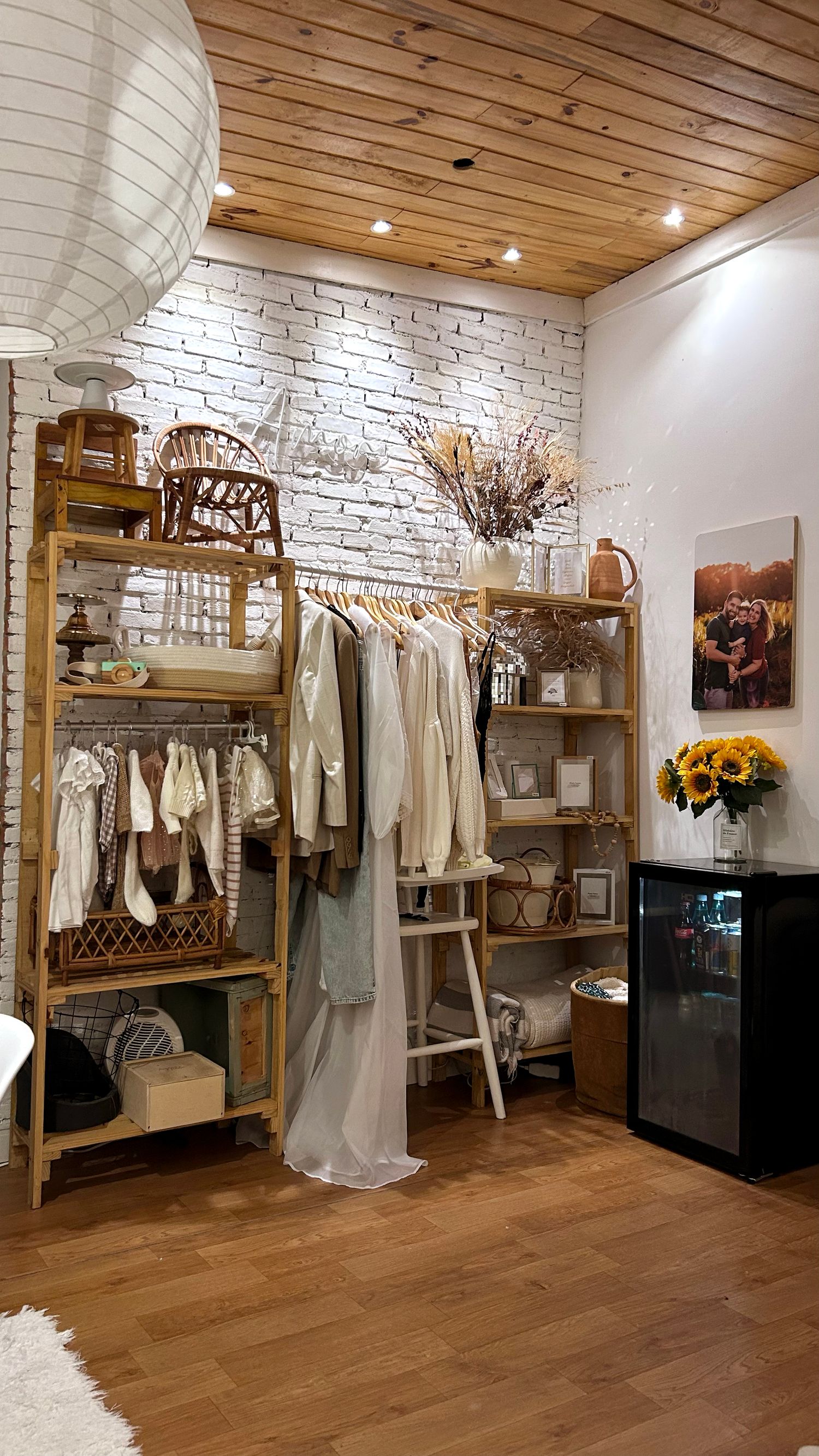 Cozy boutique corner with wooden shelving, white brick wall, clothing rack, and sunflowers in a rustic-modern retail space.