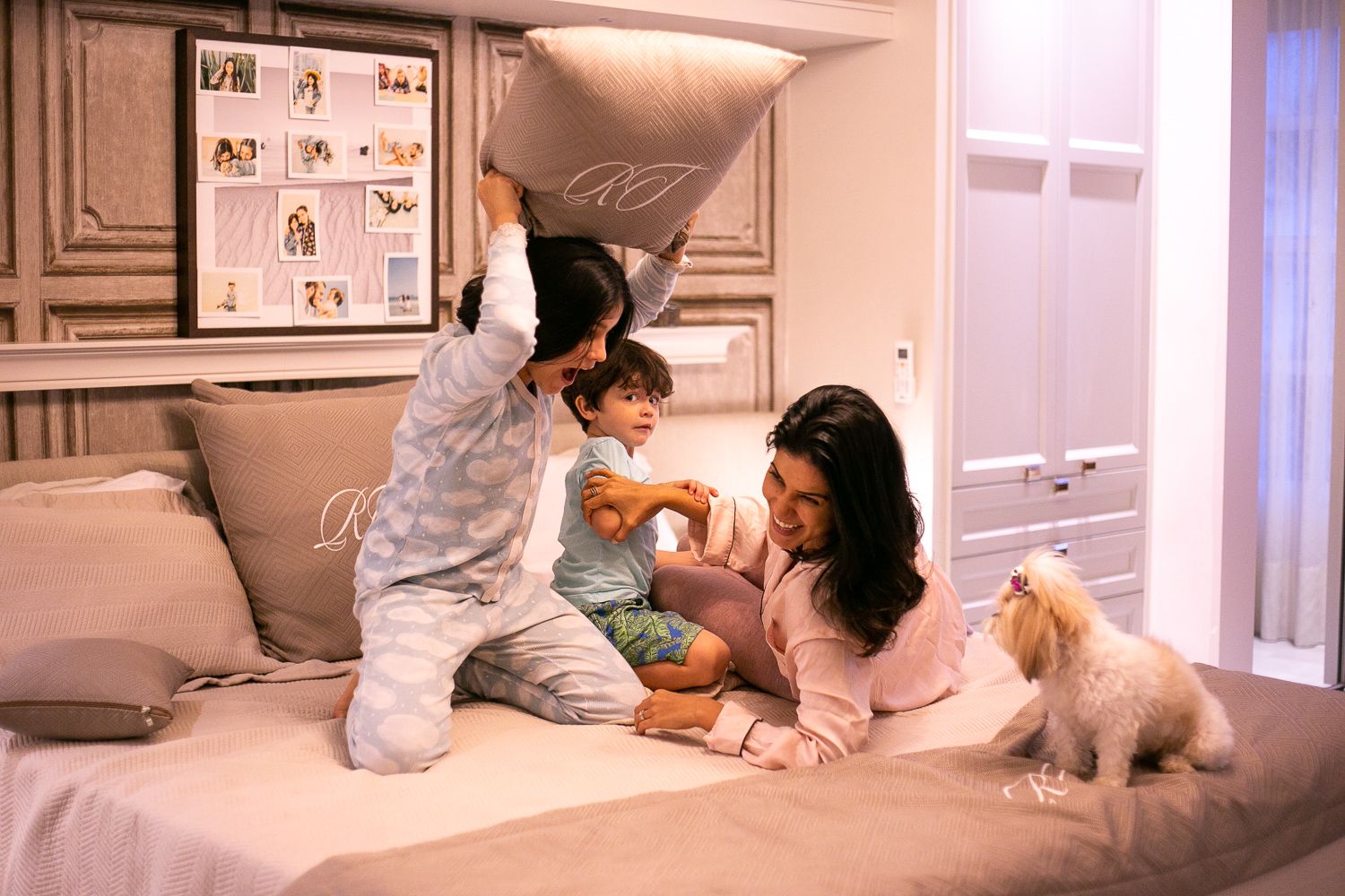 A cozy bedroom scene shows two people and a small white dog relaxing together on a bed.