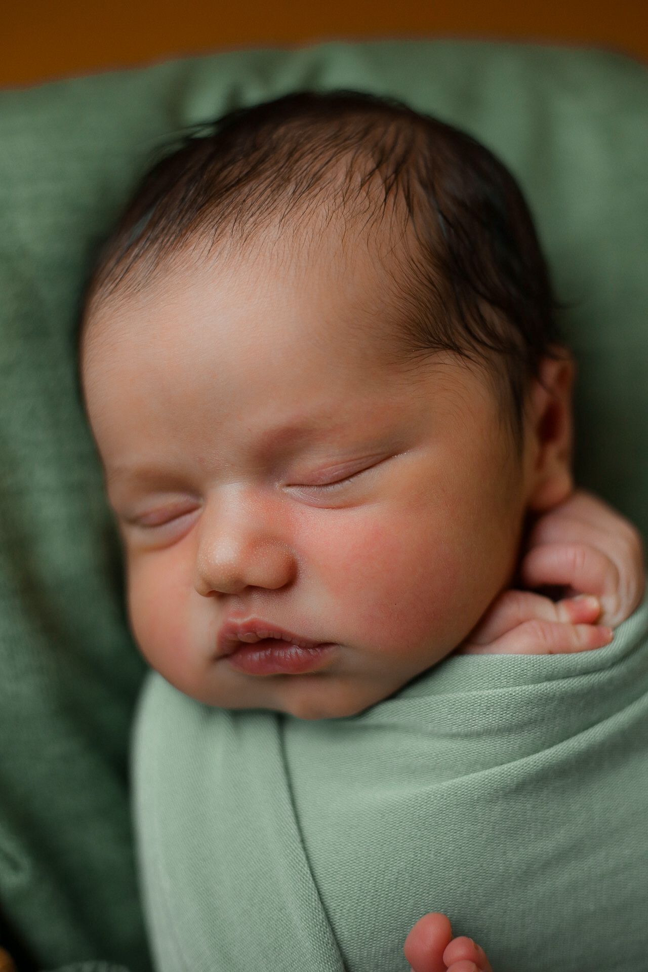 A peaceful sleeping newborn baby swaddled in soft mint green fabric.