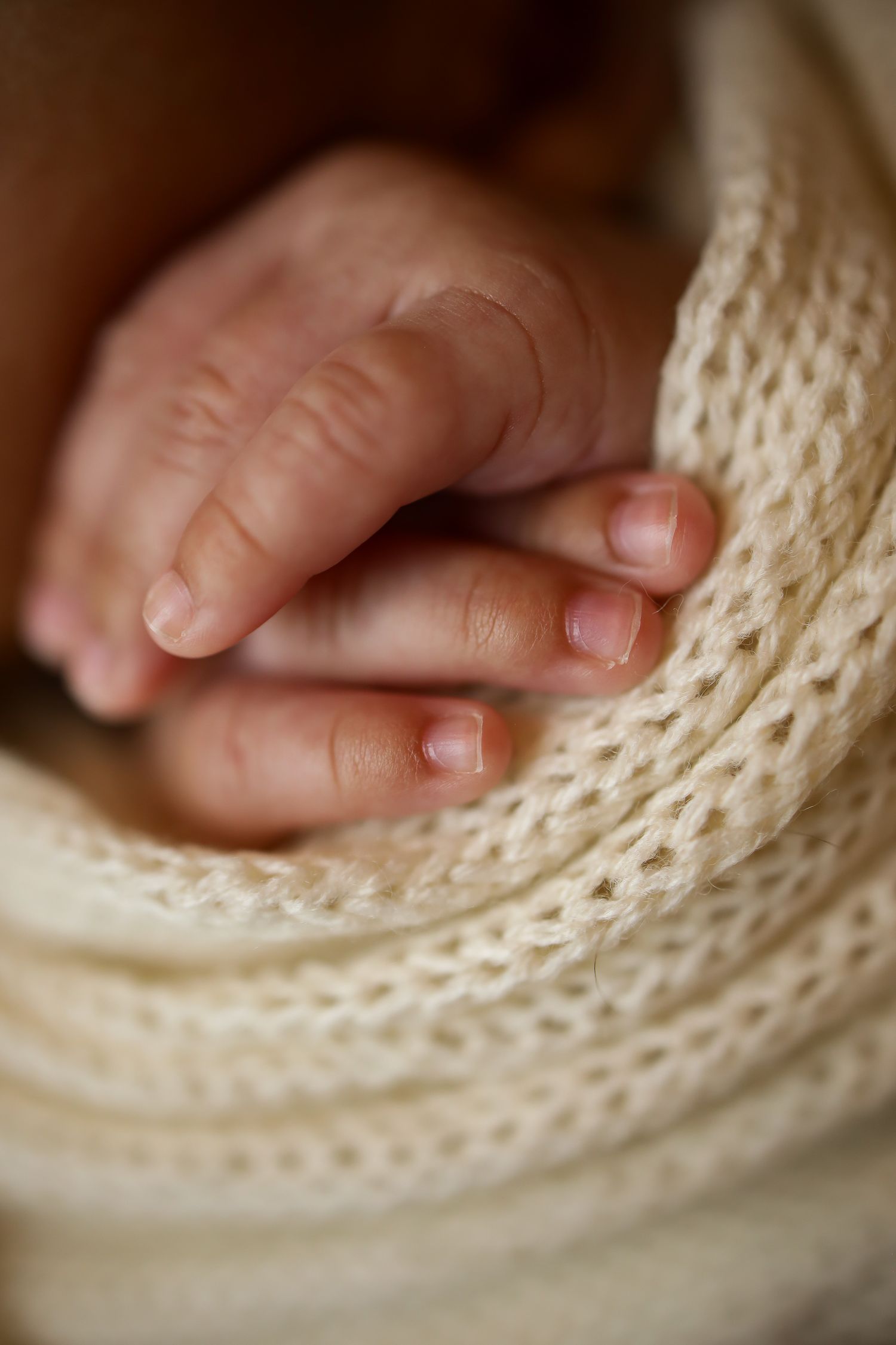 A tiny baby's hand rests gently on soft cream-colored knitted fabric, captured in macro detail.