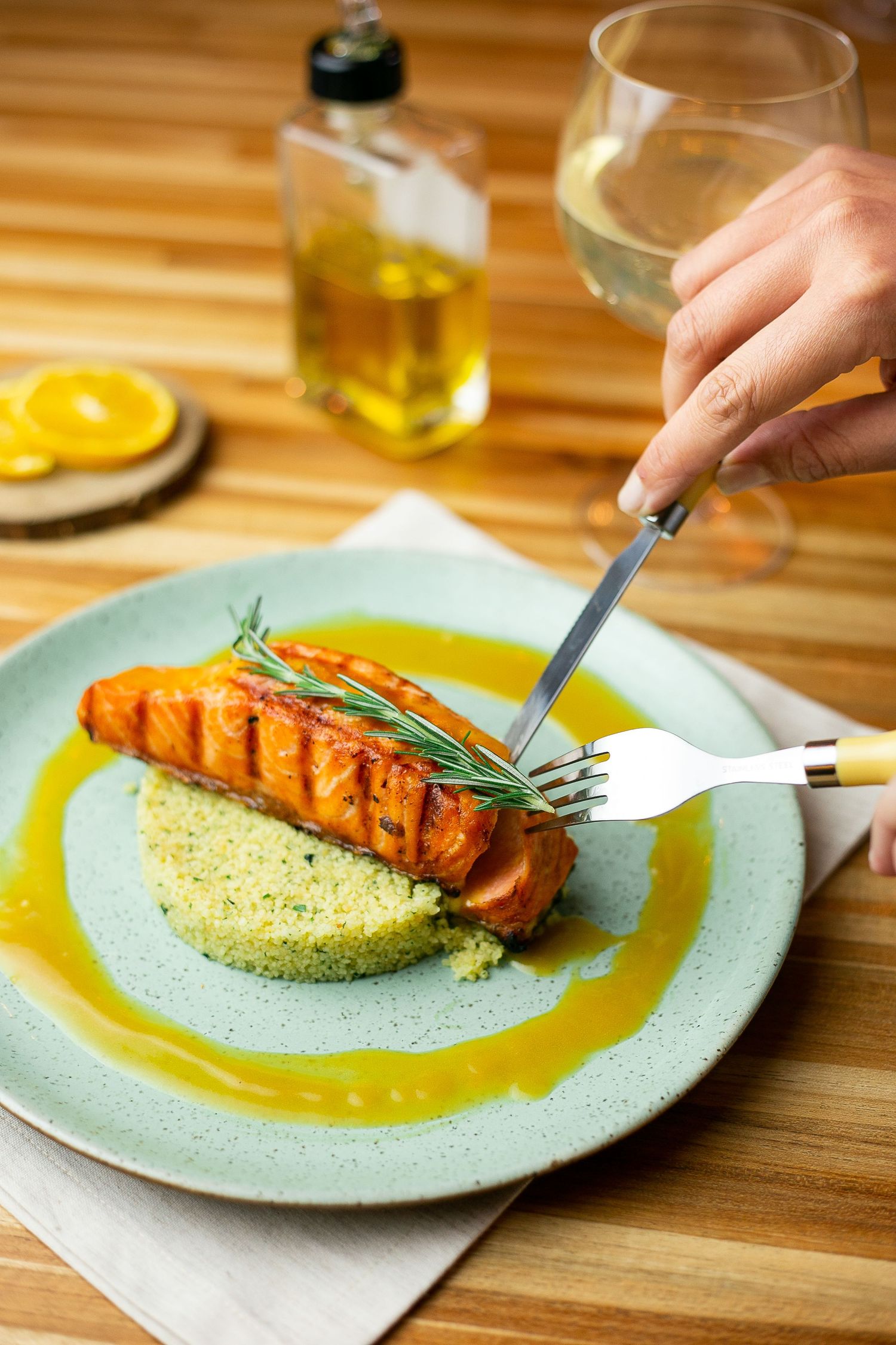 Grilled salmon fillet served on a bed of couscous with rosemary garnish and yellow sauce on a mint green plate.