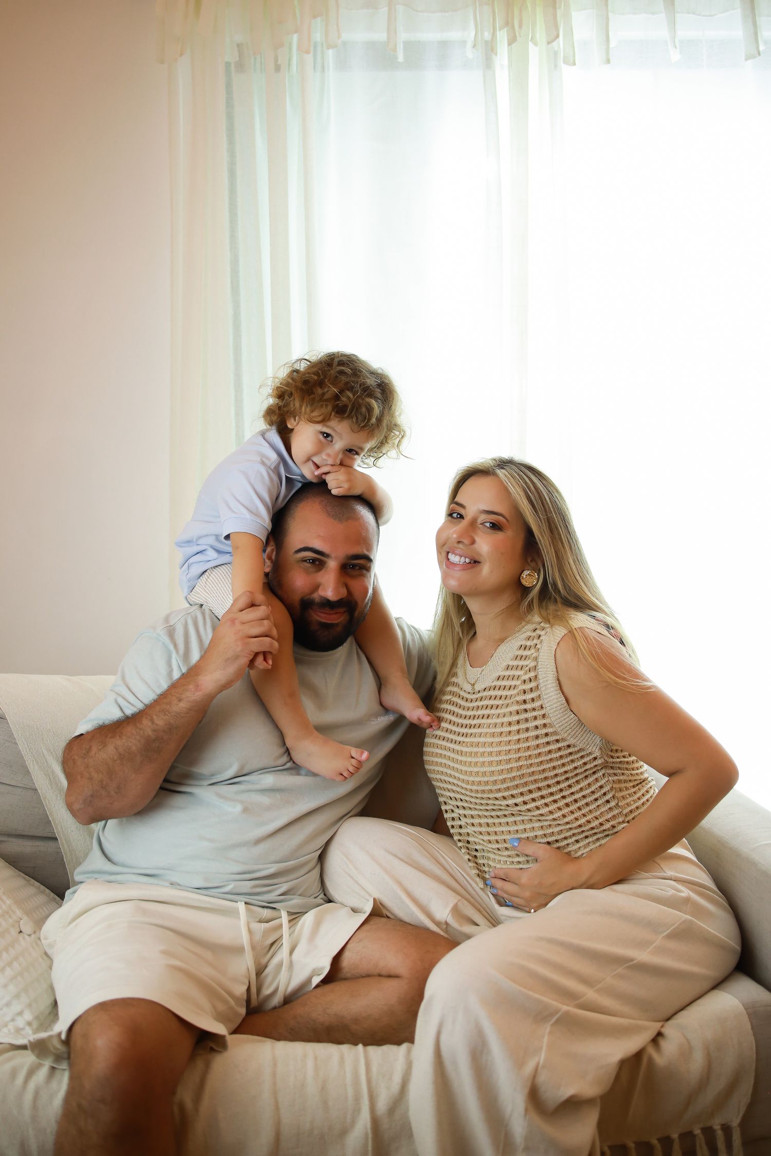 A happy family relaxes together on a bright white couch near a sunlit window.