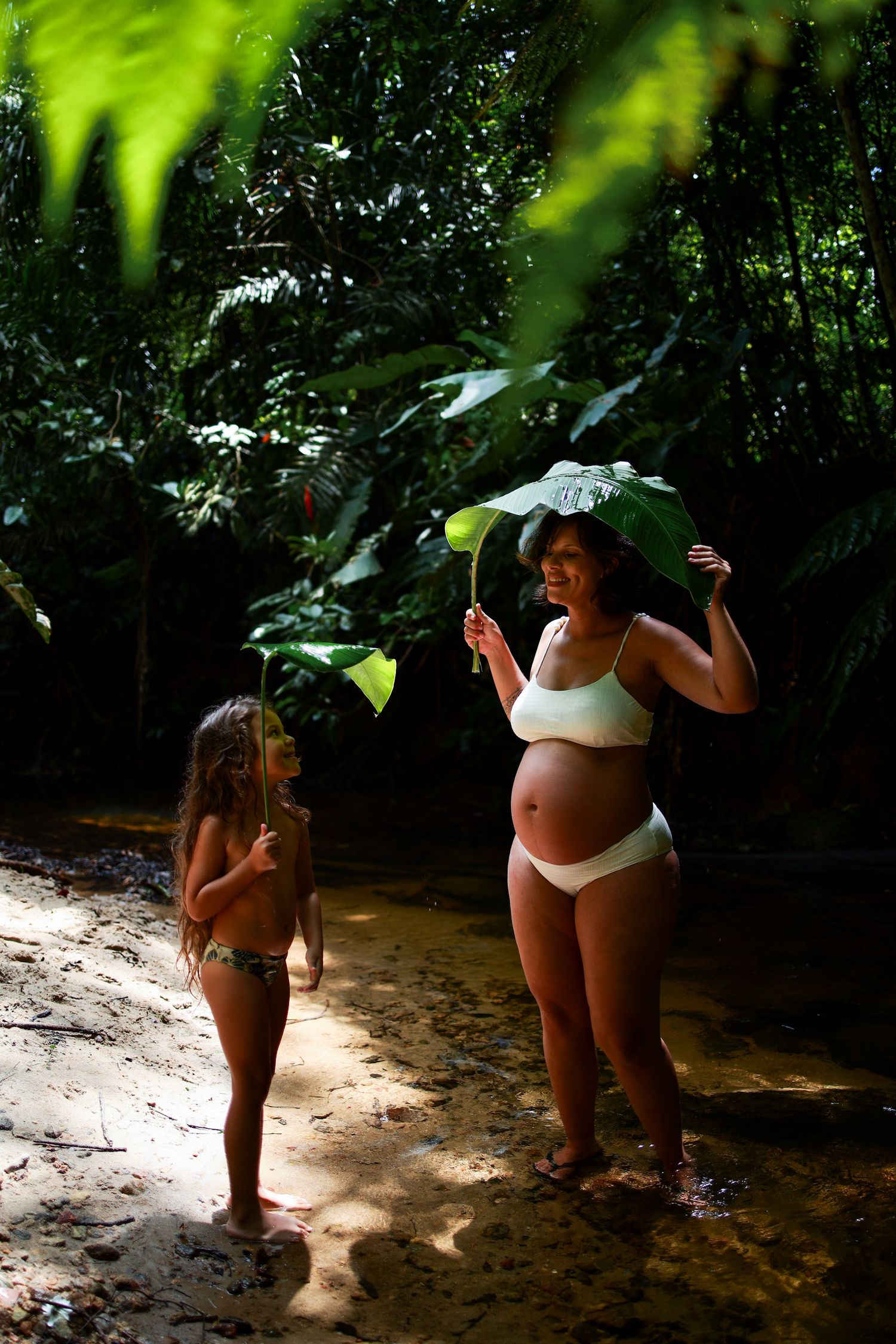 Two people stand in a shallow stream surrounded by lush tropical foliage and dappled sunlight.