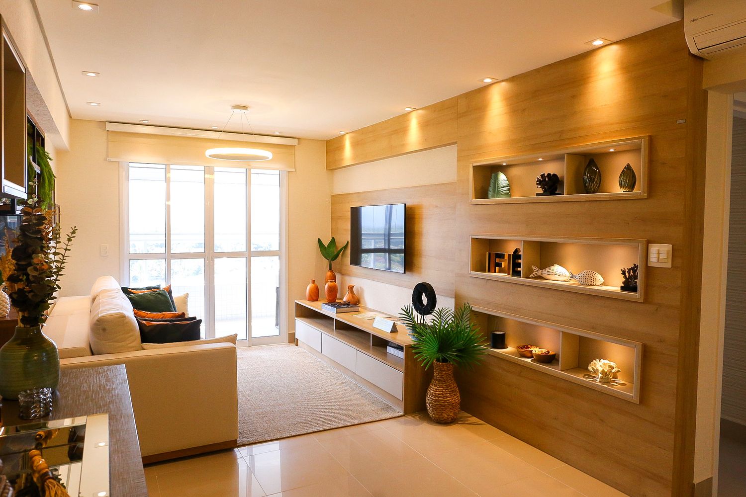 Modern living room interior with wooden wall panels, built-in TV unit, beige sofa, and decorative display shelves.
