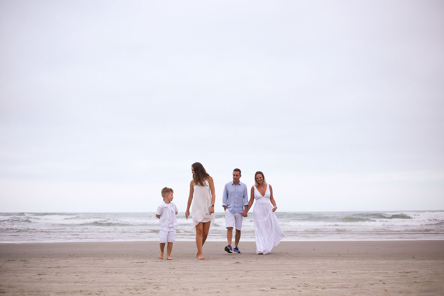 A family wearing white clothing walks together along a peaceful beach at sunset.