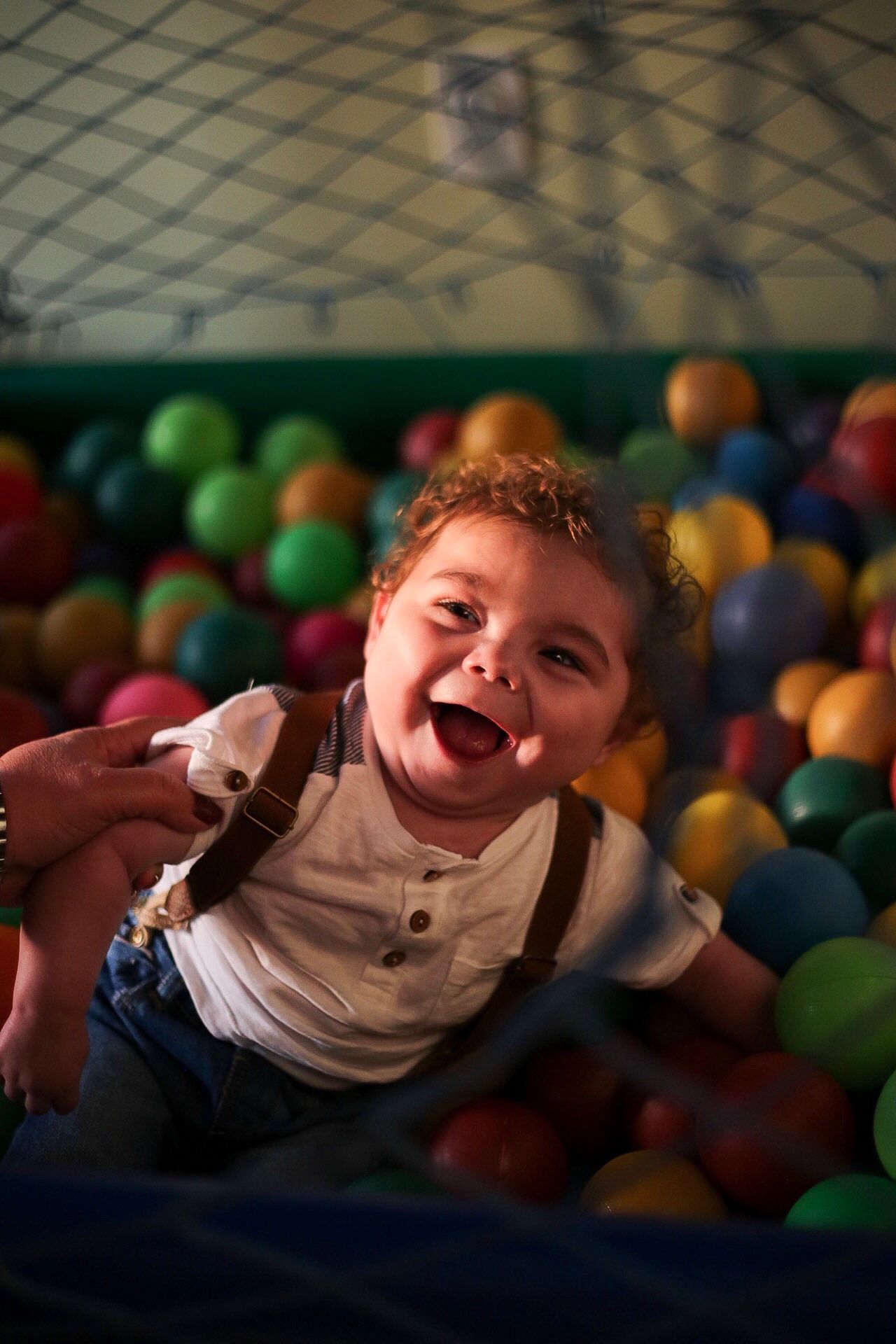 Child laughs with joy while playing in a colorful ball pit at an indoor playground.