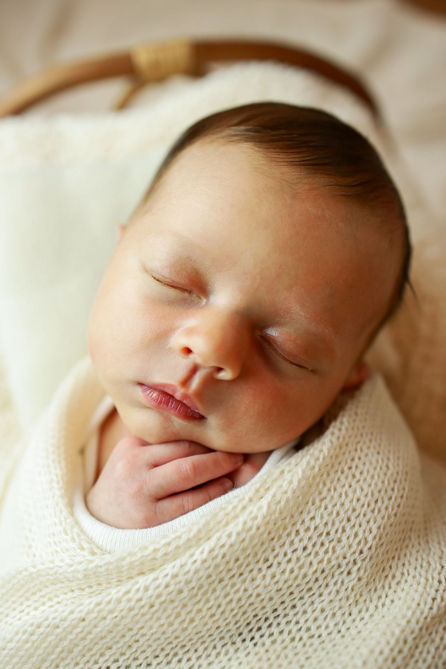 Peaceful sleeping infant swaddled in soft white knit blanket during newborn photoshoot.