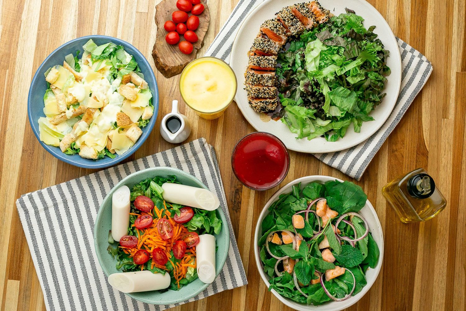 Overhead view of healthy meal spread featuring grilled meat, salads, pasta, and colorful vegetables on wooden table.