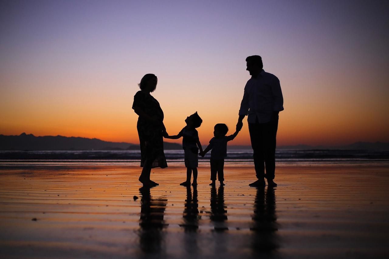 Silhouette of a family of four holding hands on a beach during golden sunset hour.