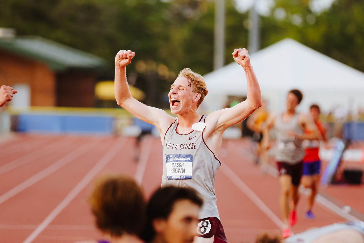 Athletes celebrate with raised arms and expressions of joy after competing on an outdoor track field.
