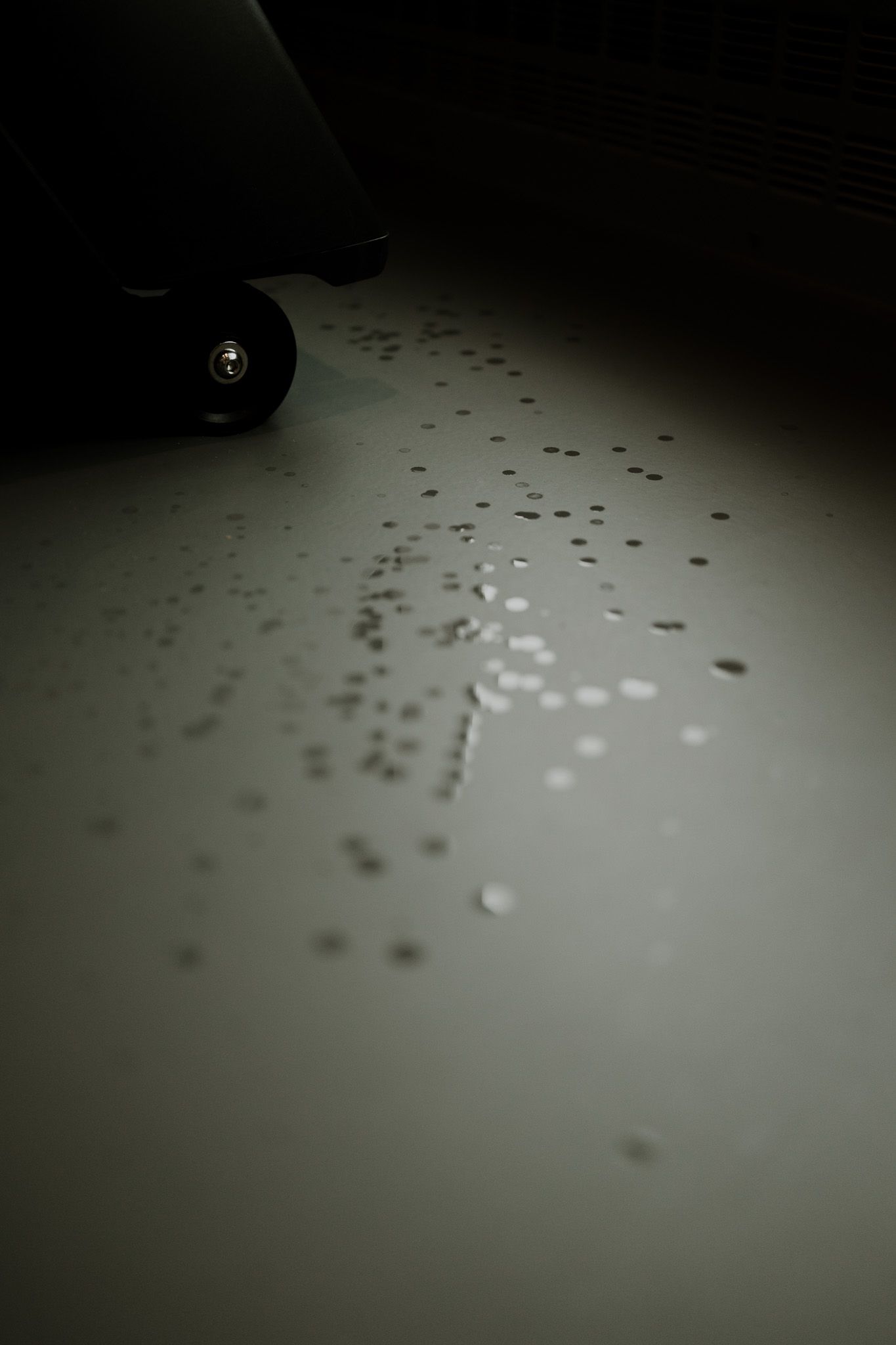 Small white droplets scattered across a dark surface create a pattern in dim lighting.