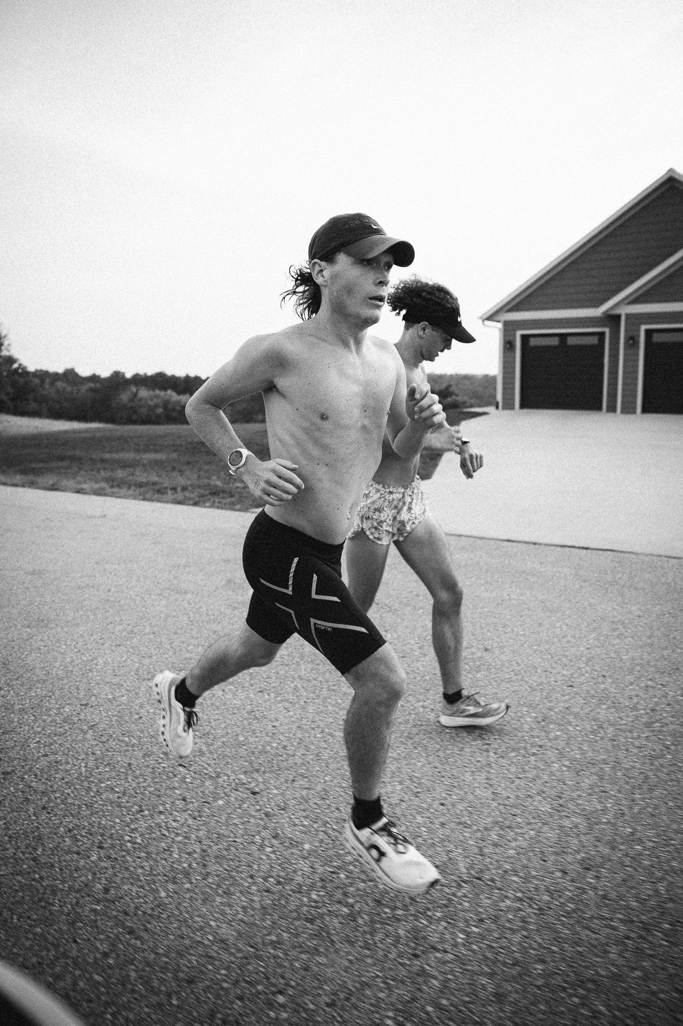 Black and white sequence of a shirtless skateboarder performing tricks on a paved surface near buildings.