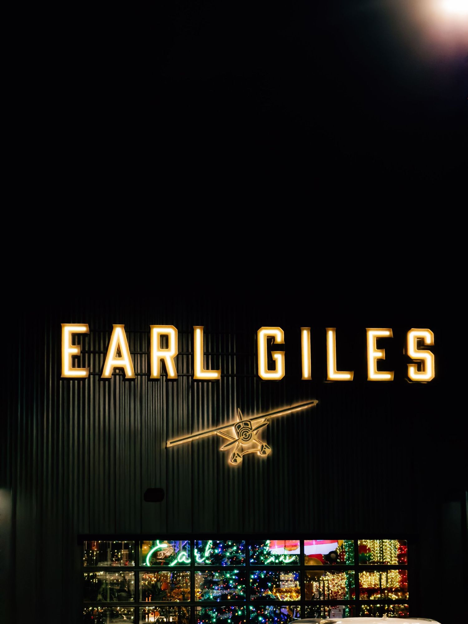 Illuminated Earl Giles sign with golden airplane silhouette mounted on dark building exterior at night.